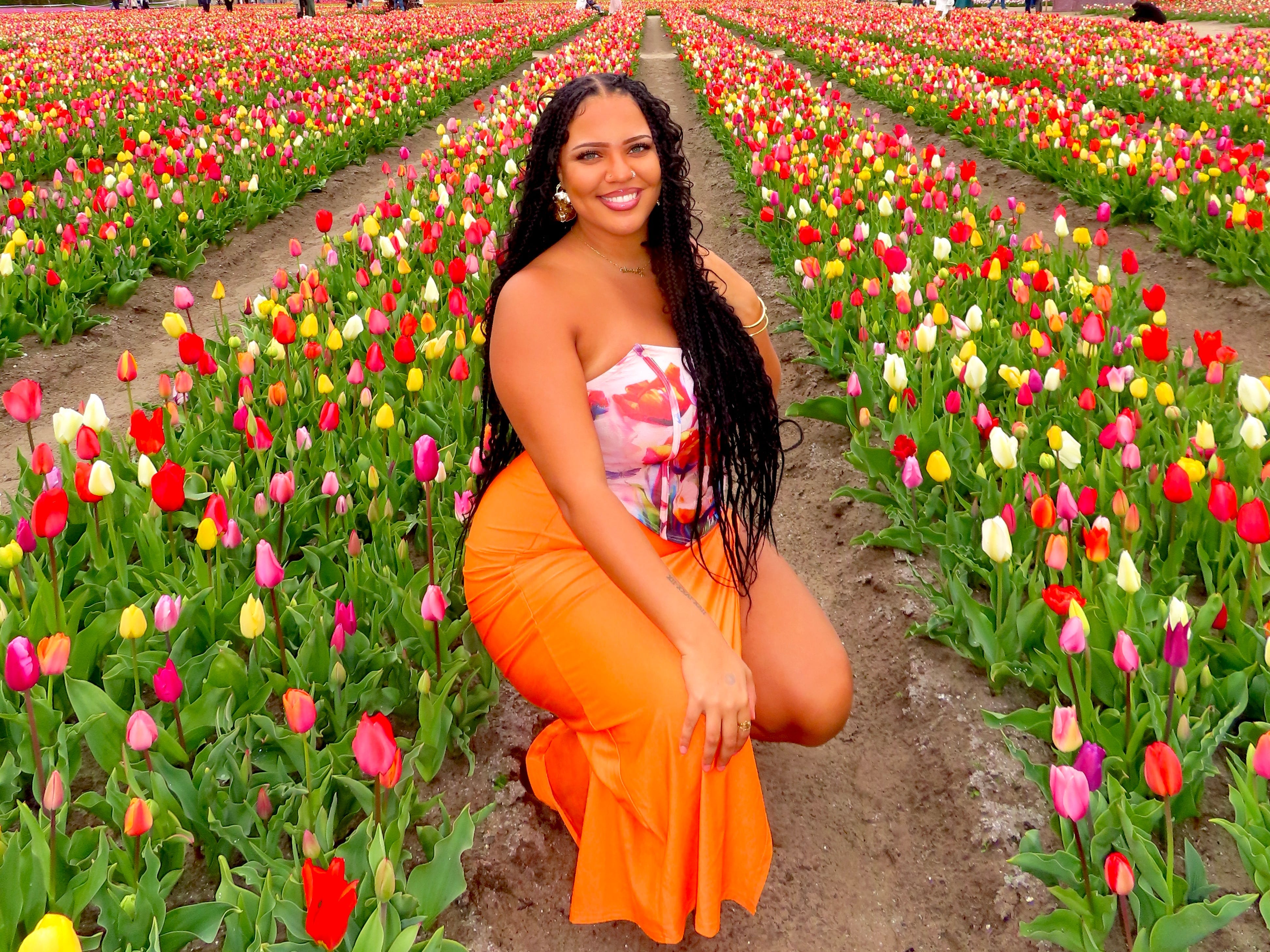 Jasmin kneels down between rows of thousands of colorful tulips.