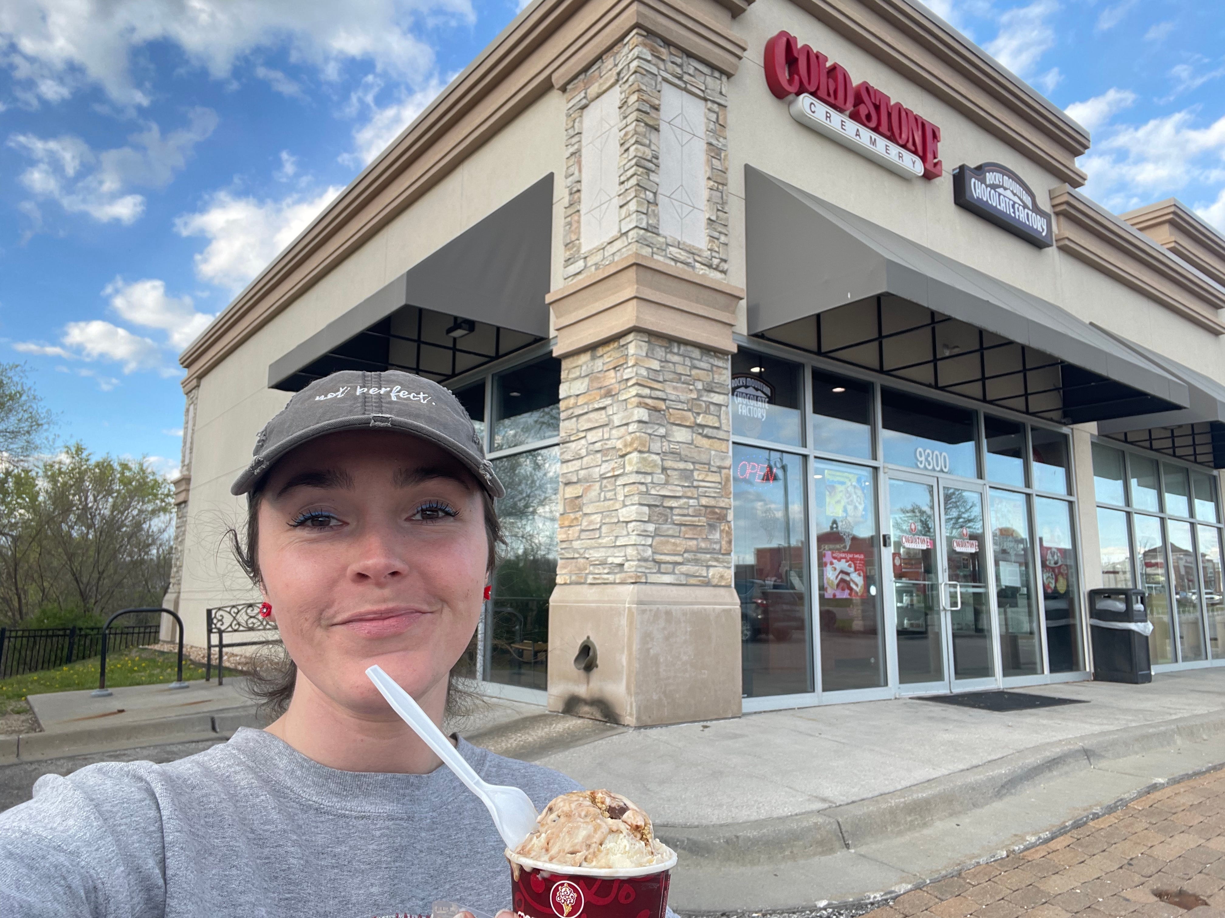 The author outside a Cold Stone Creamery wearing a hat and holding one of the cups of ice cream.
