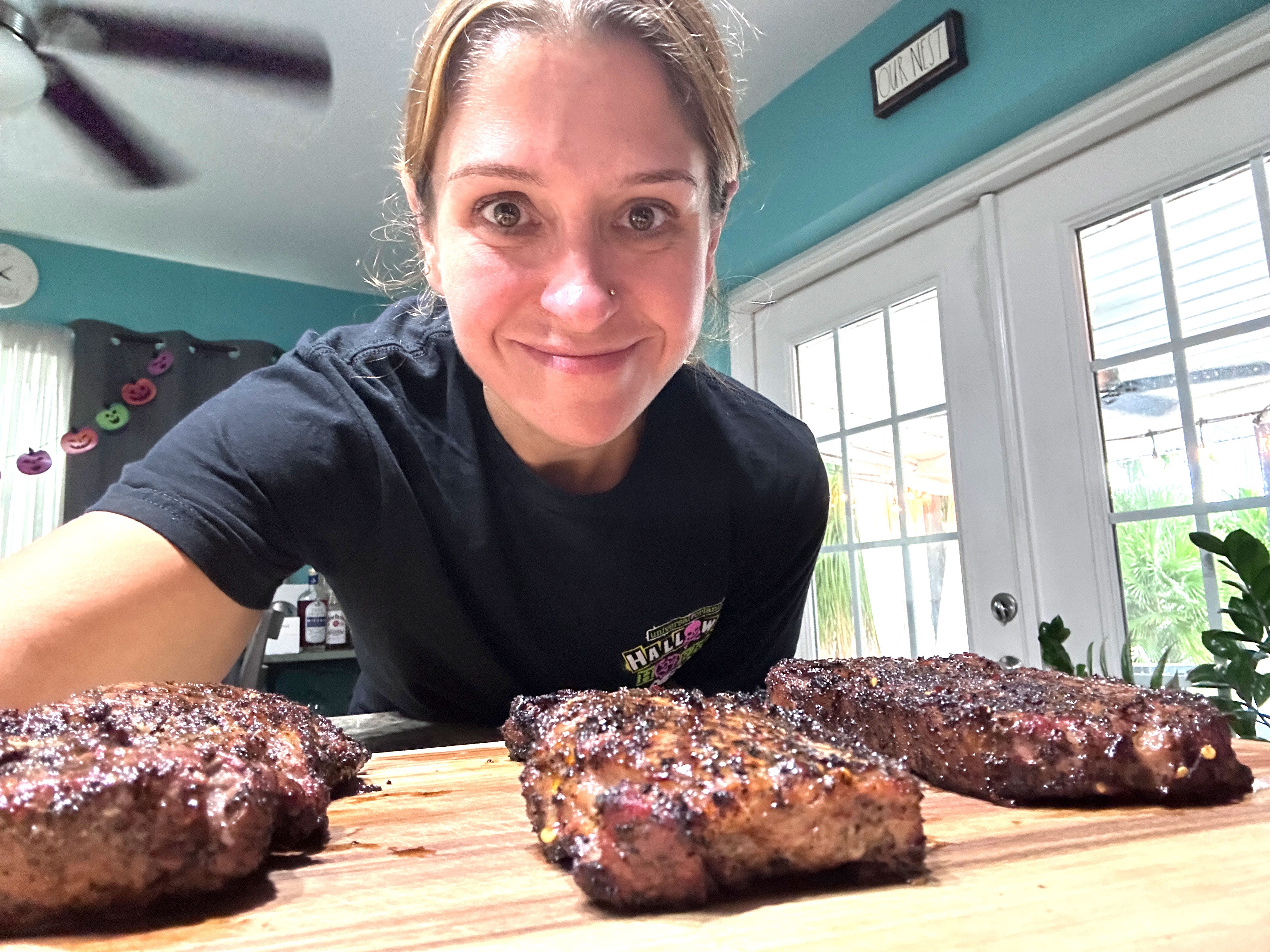 The author leans over three pieces of cooked steak on a cutting board.