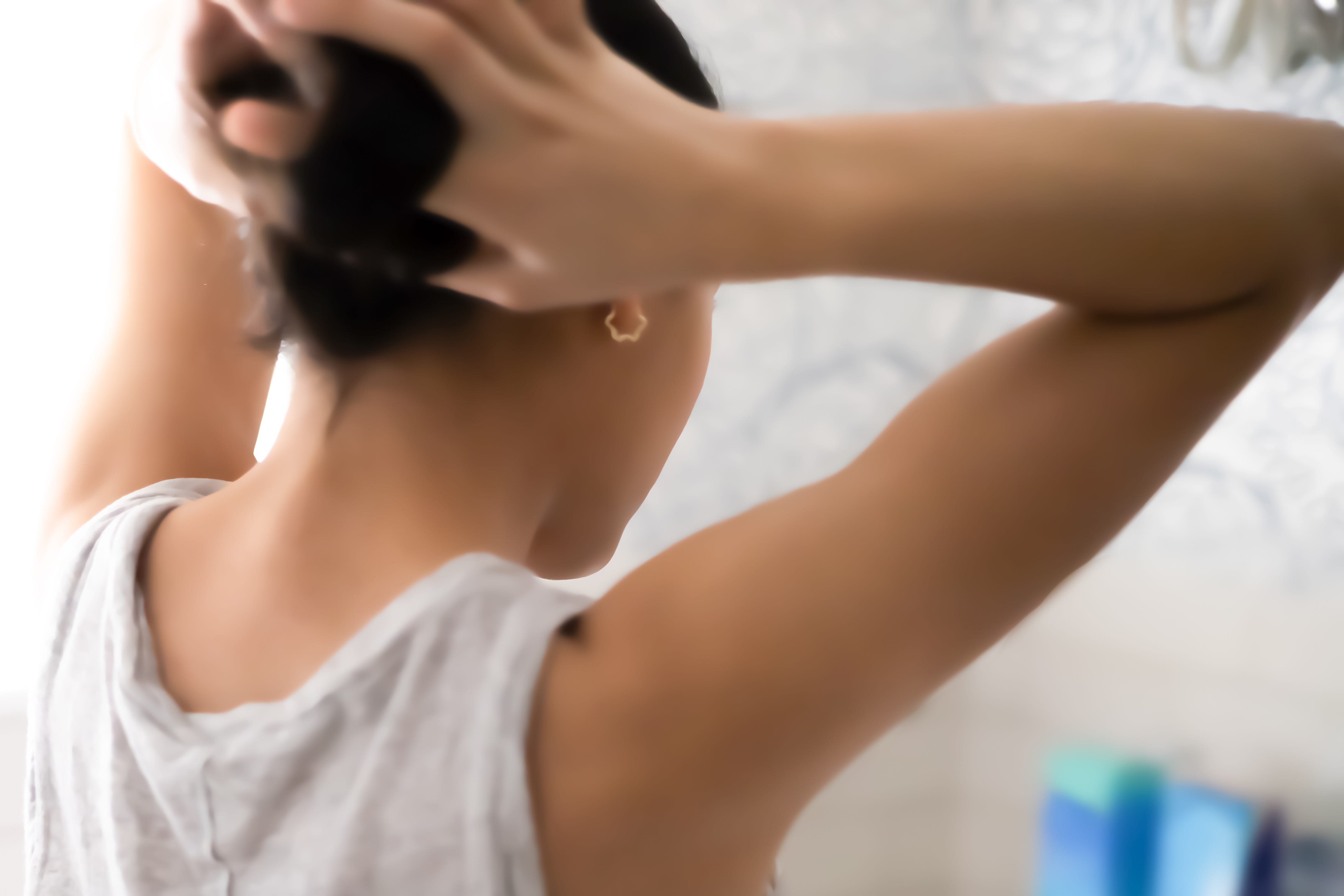 Mixed-race female standing in front of bathroom mirror putting hair in ponytail