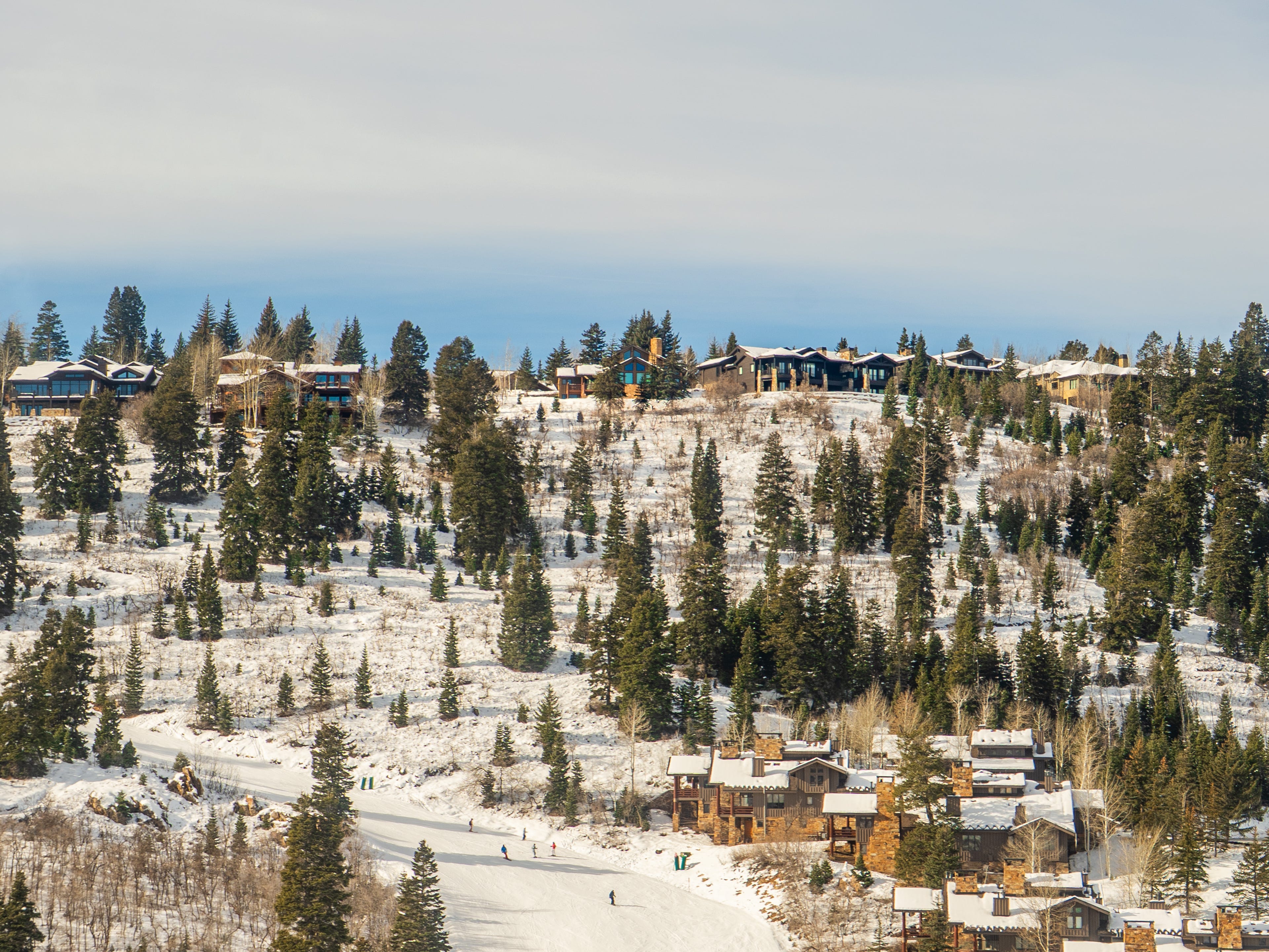 Condos, mansions, and trees line a snowcapped mountain in Park City, Utah, with skiers gliding down the slopes