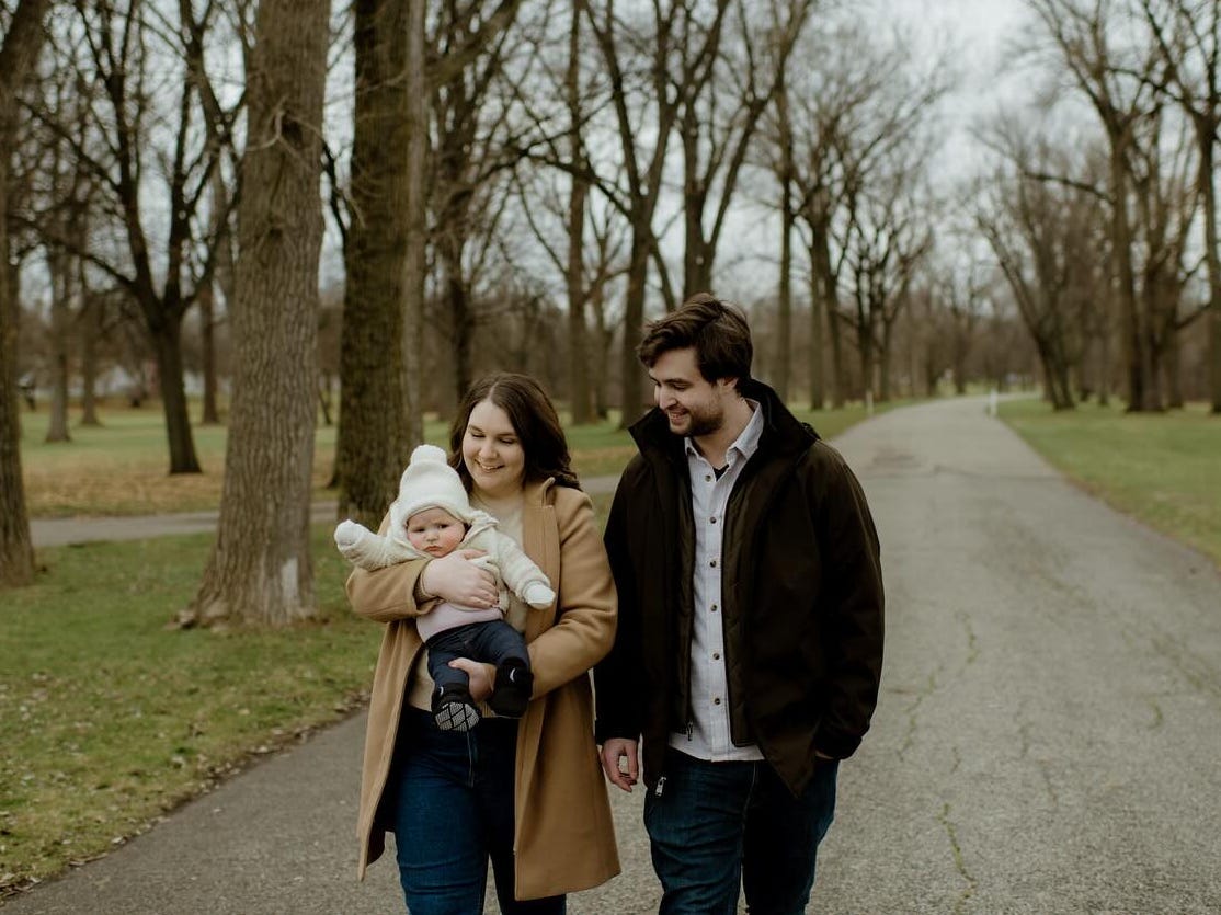 The author holding her baby while walking down a path, her husband is standing next to her.