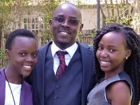 A man in a suit poses with his two daughters.