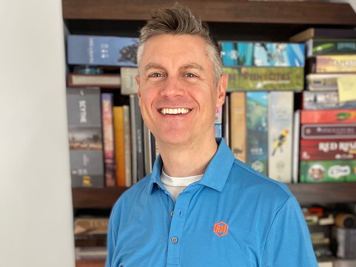headshot of a man in a blue shirt in front of board games