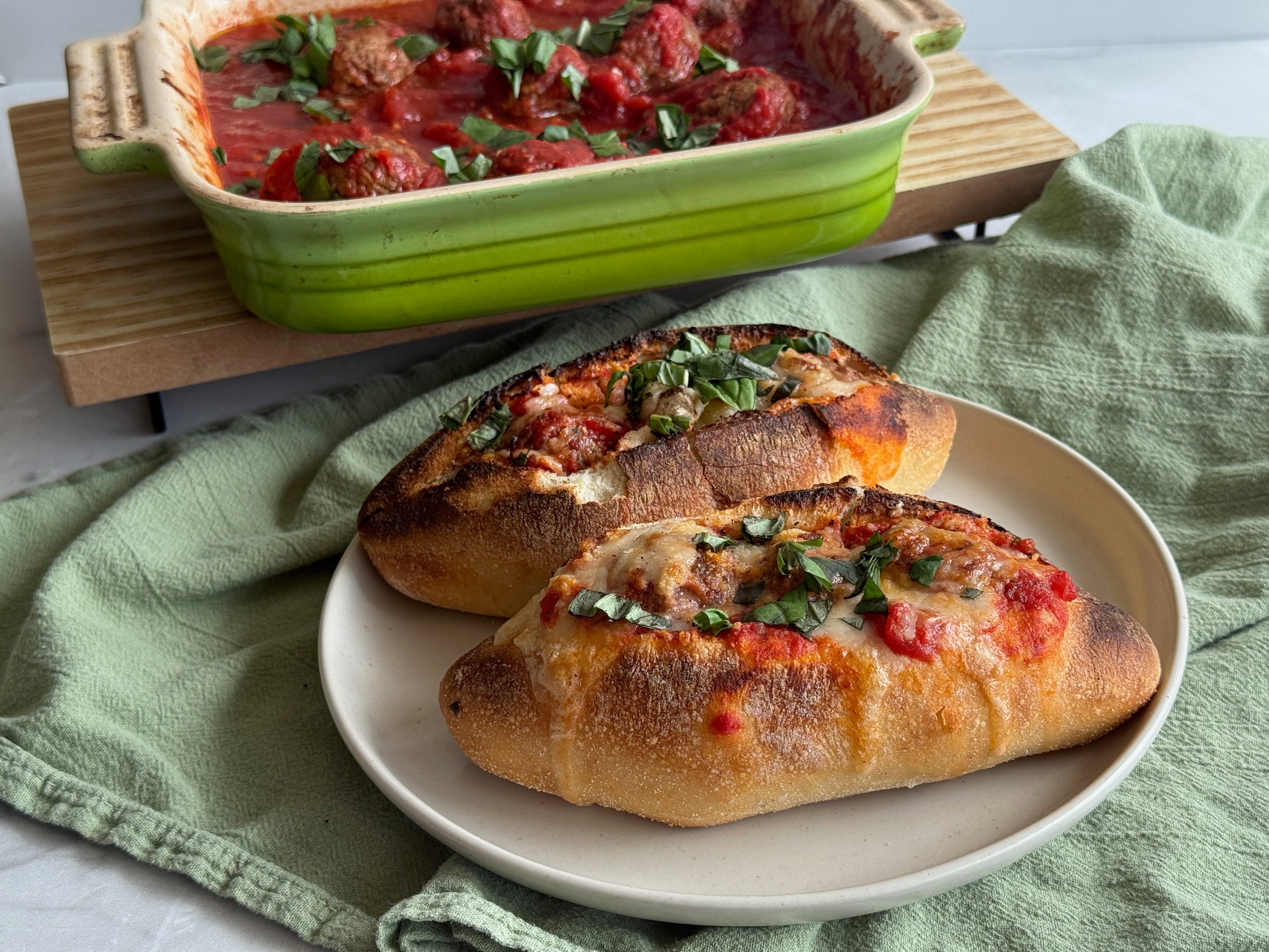 A casserole of meatballs and two meatball sandwiches on display.