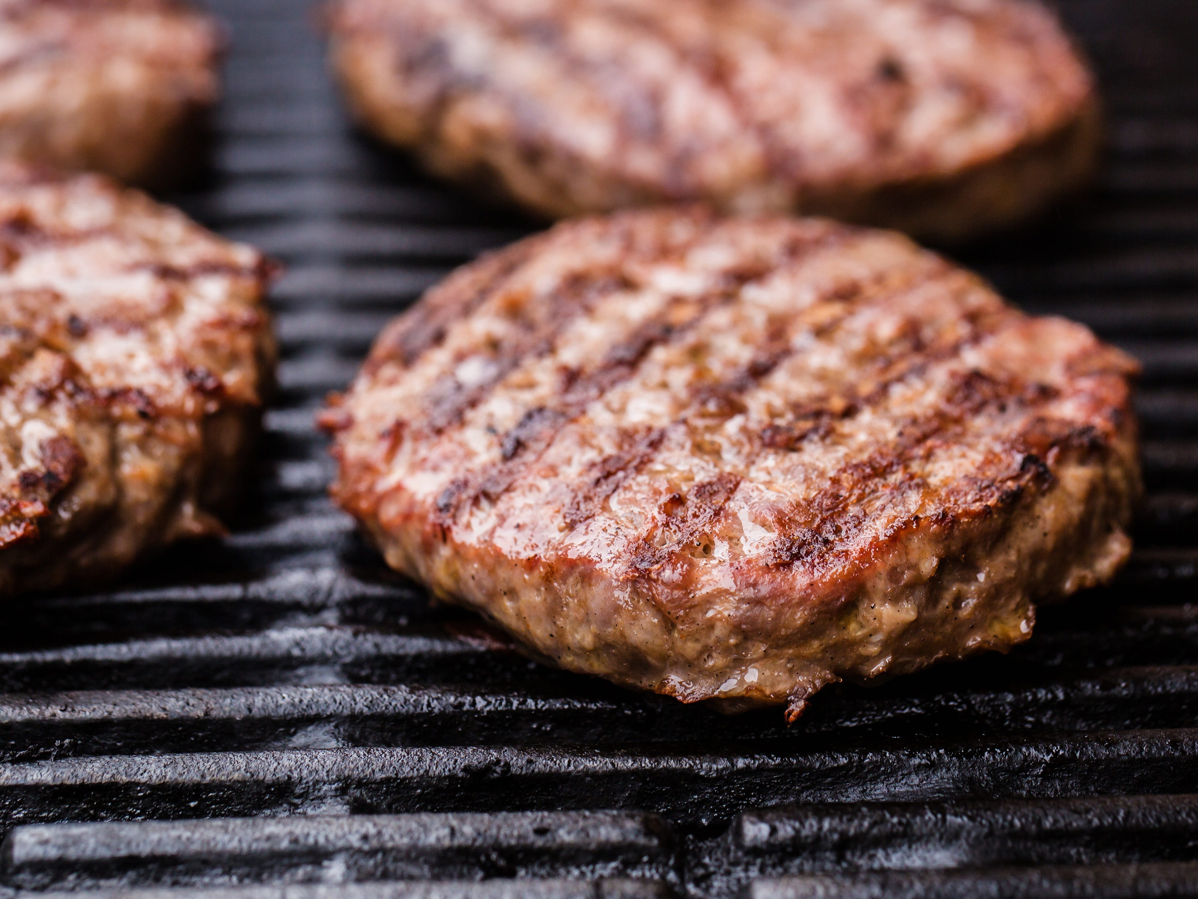 Four burger patties with grill marks on a grill