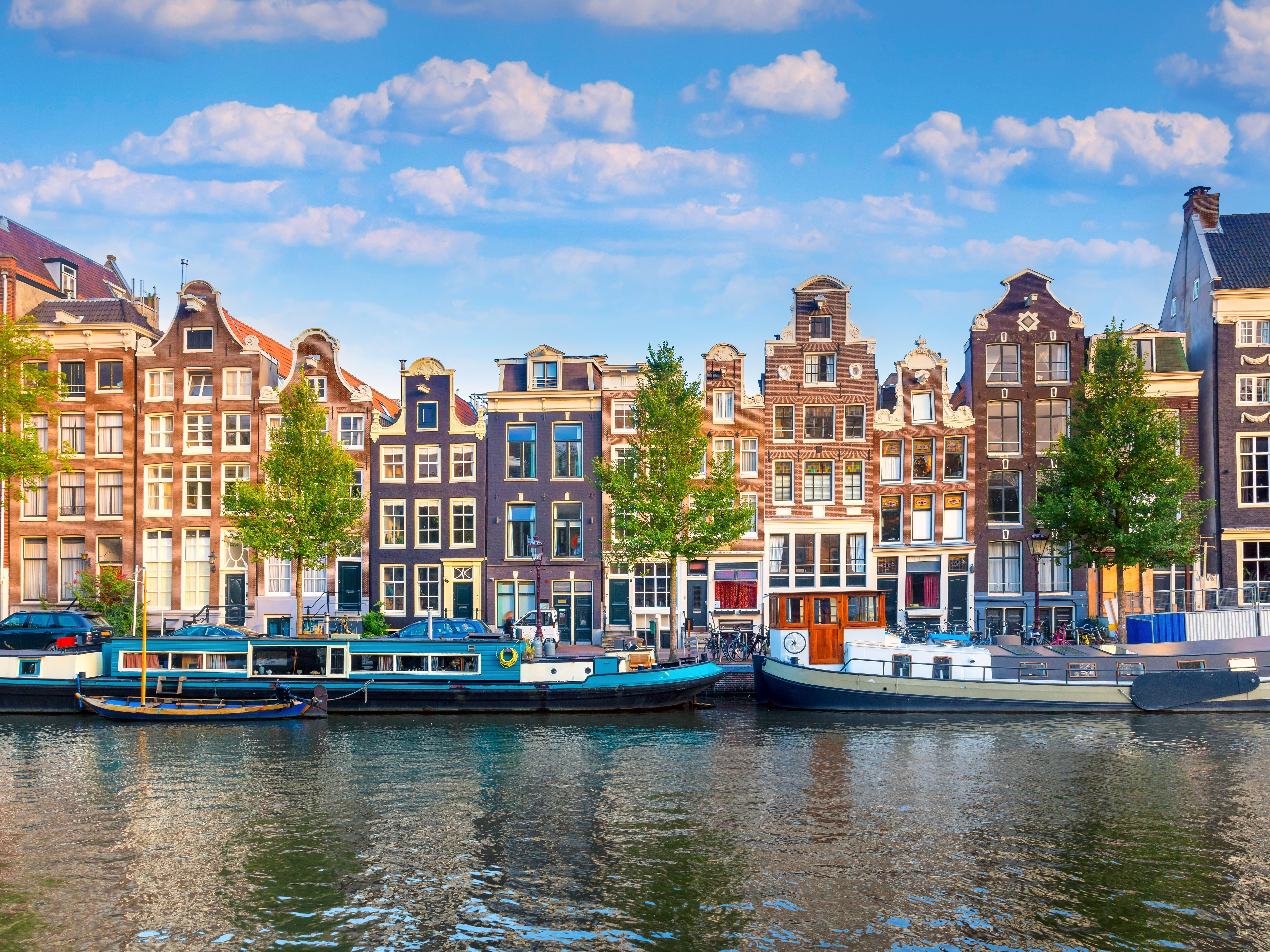 A row of houses in Amsterdam. The canal is in the foreground with docked boats.