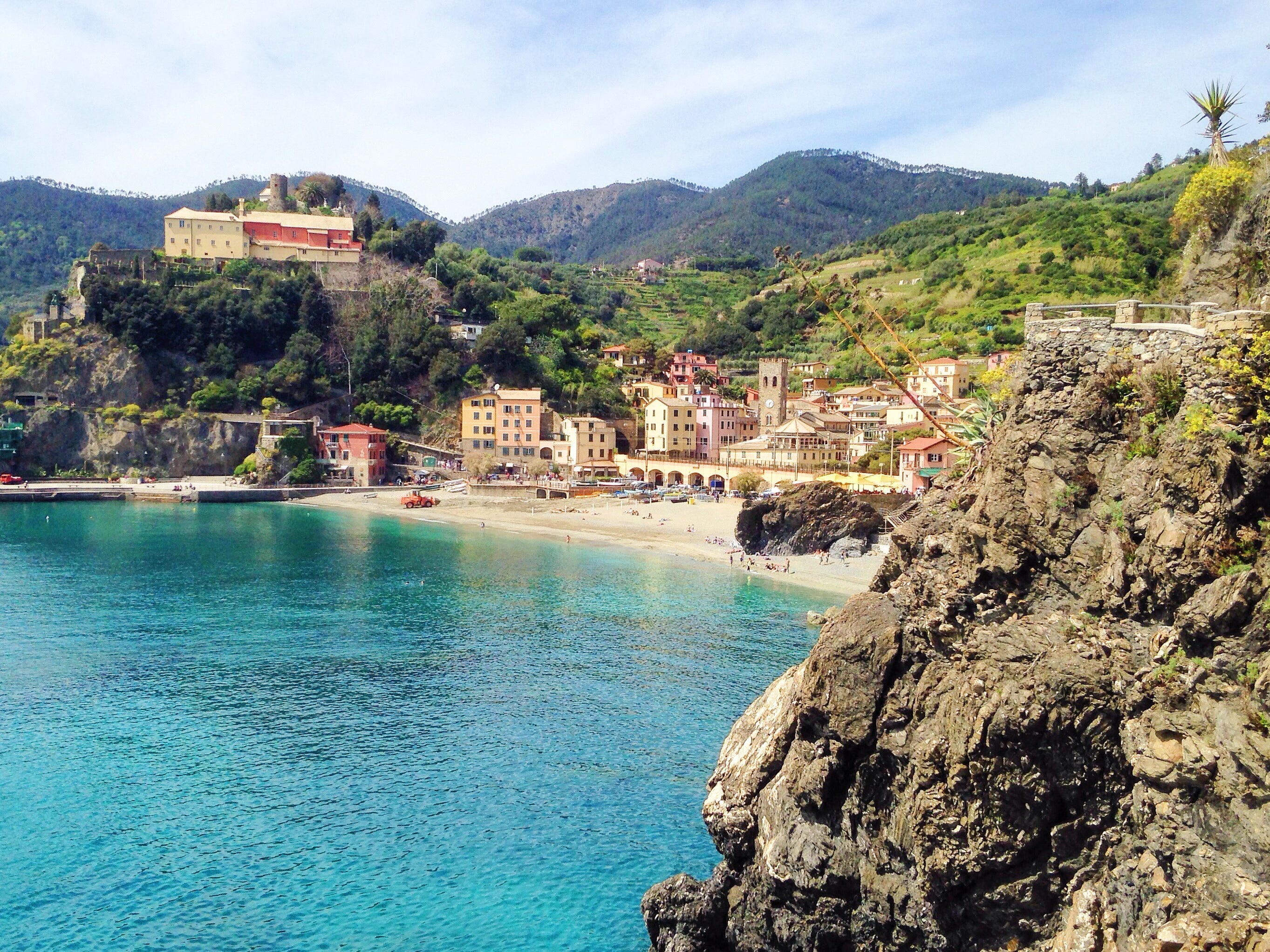 The view of a seaside town with colorful buildings and tall cliffs from a hiking trail.