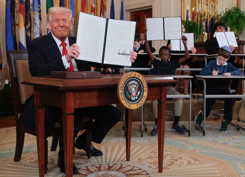 Joined by children seated at school desks, U.S. President Donald Trump holds up the signed executive order to gut the Education Department