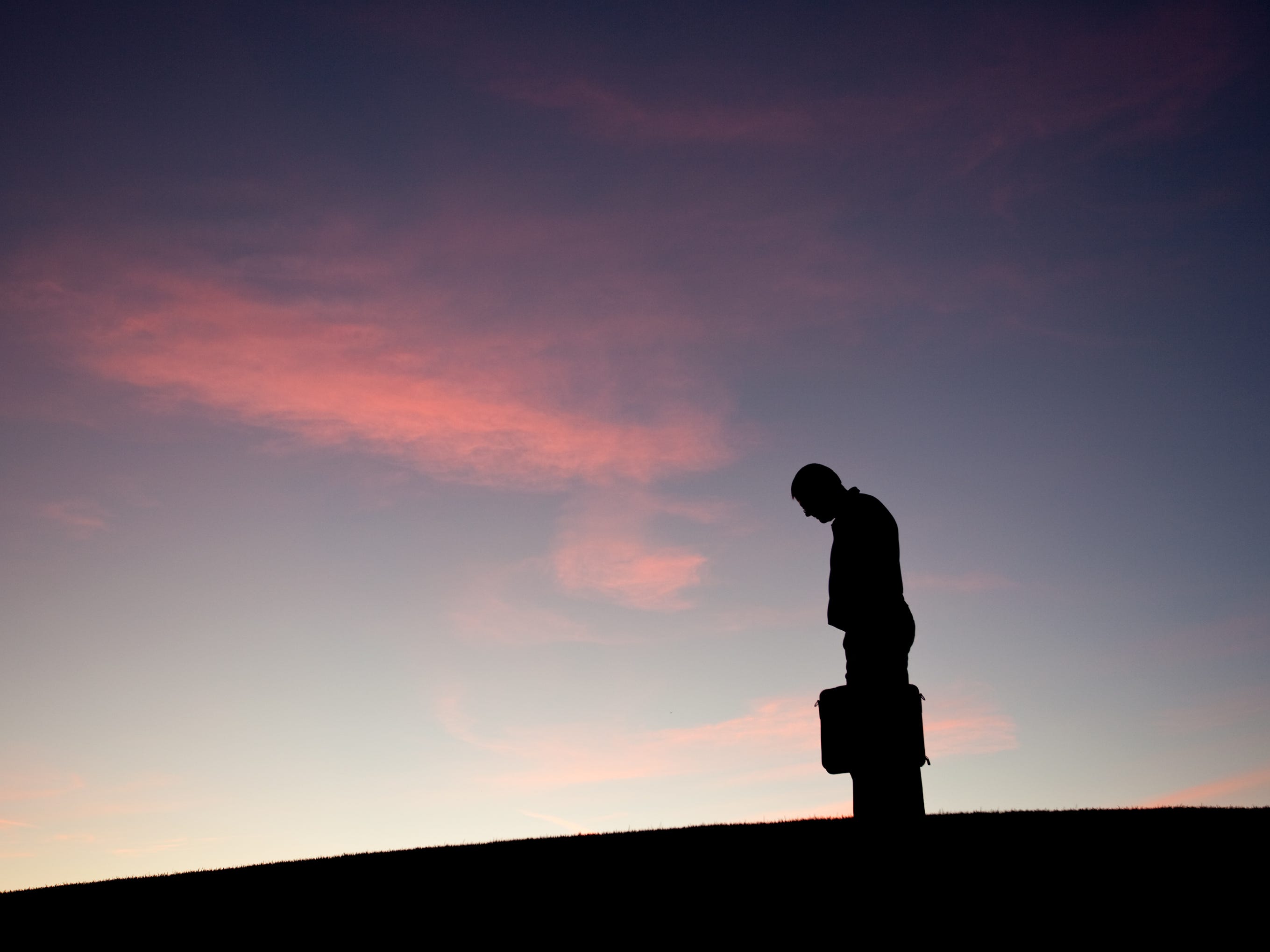 The silhouette of a businessman hanging his head low in sadness.