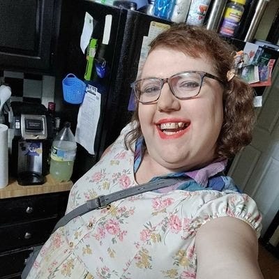 A trans woman smiles in front of a kitchen counter.