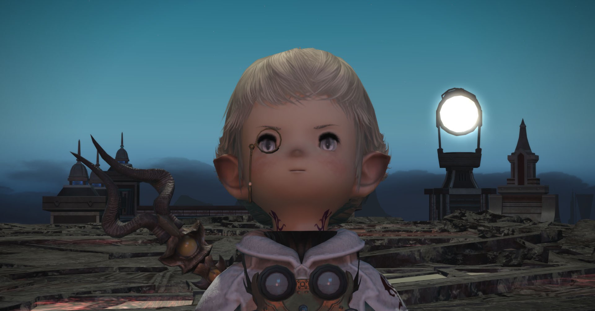 Papalymo, a small being with elf ears and a monocle, stands in front of a series of strange stone structures