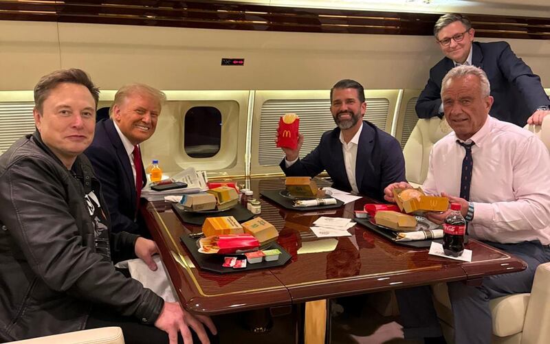 Health nut Robert F. Kennedy (right) reluctantly smiles with a McDonald’s meal shortly after Donald Trump’s election win.