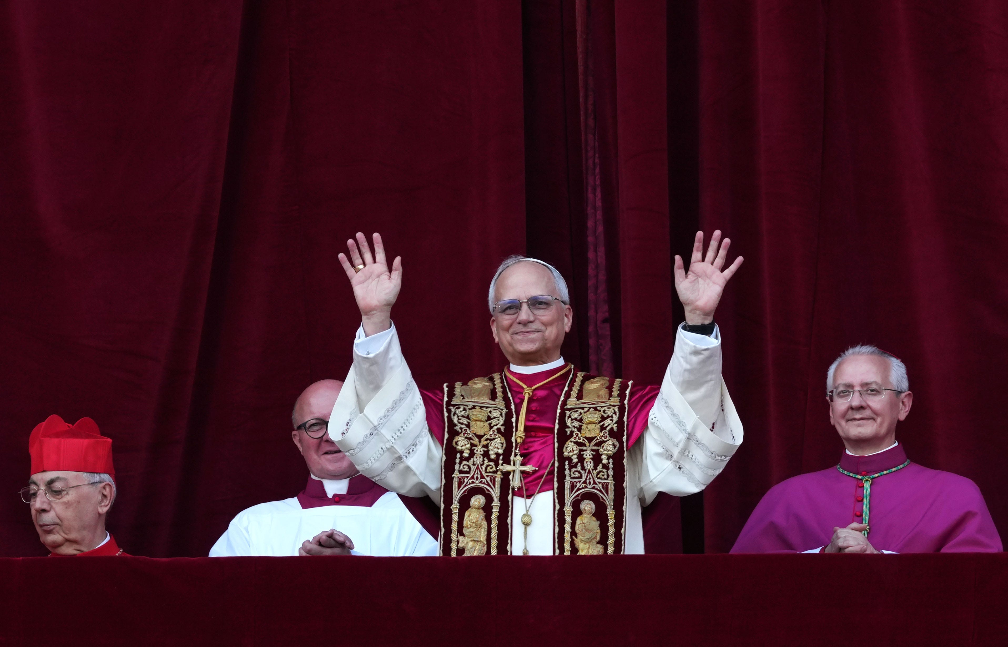Pope Leo XIV holds two hands up with cardinals standing next to him
