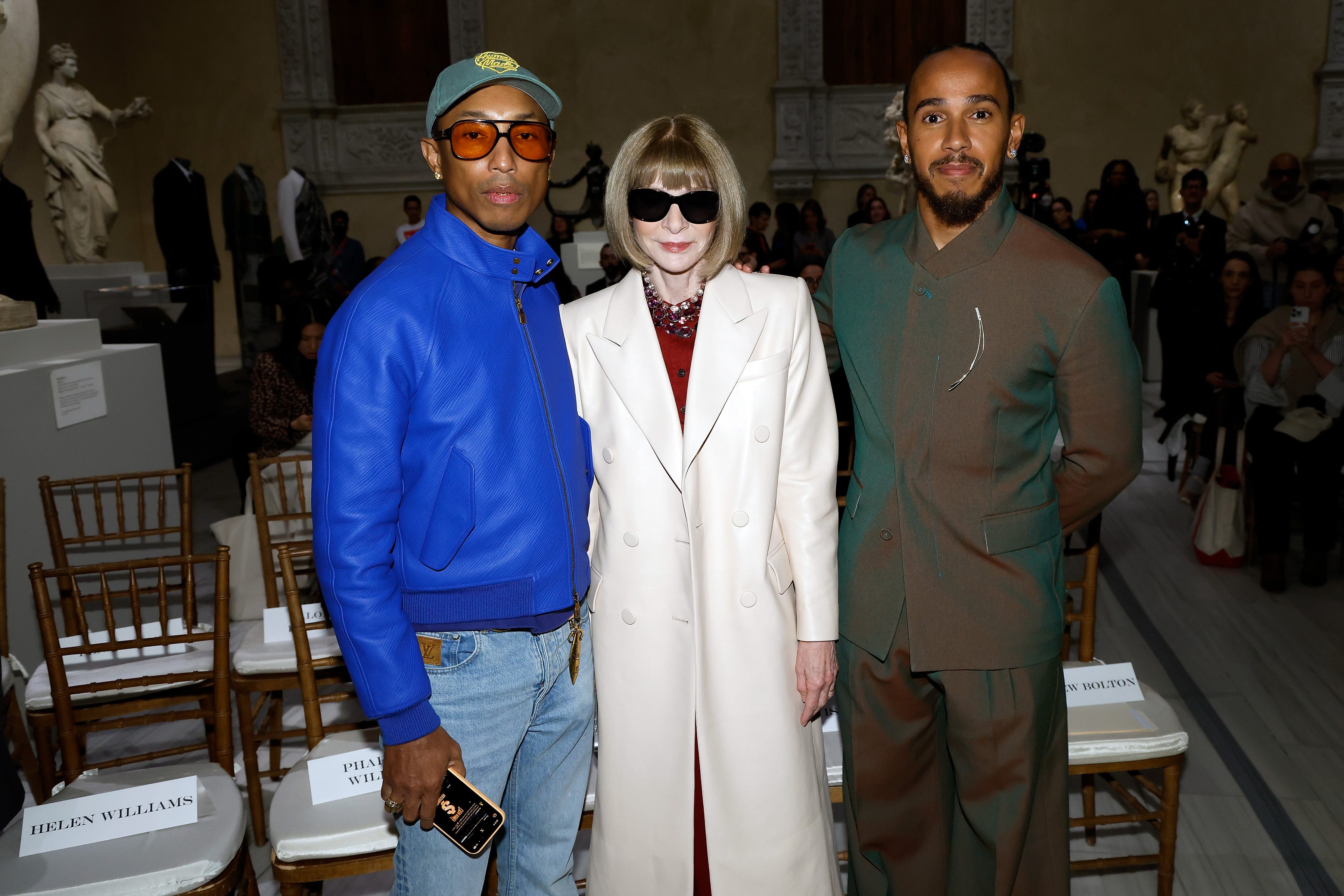 Pharrell Williams standing with Anna Wintour and  Lewis Hamilton