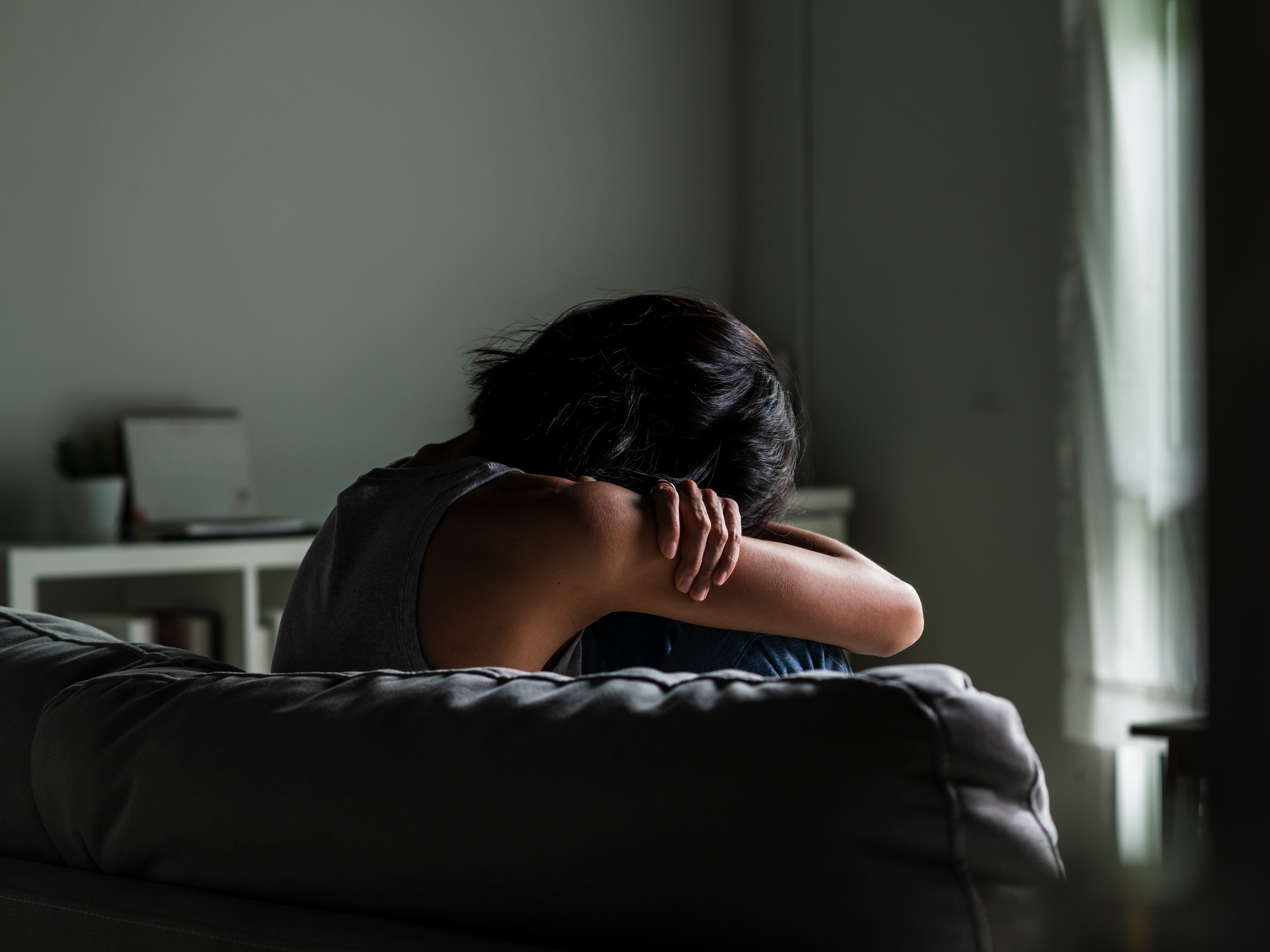 Woman sitting on couch with her head on her knees, looking sad.