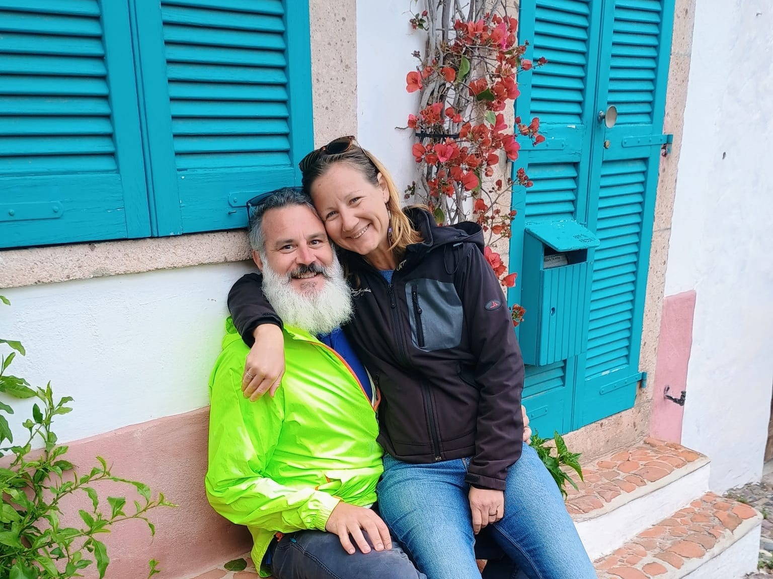The author and her husband in Italy, sitting on a bench in front of a house with blue shutters.