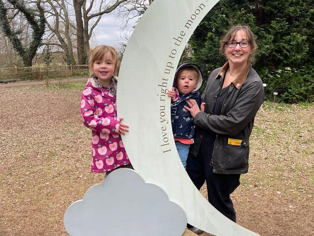 A woman poses with her two children by a sign shaped like a moon.
