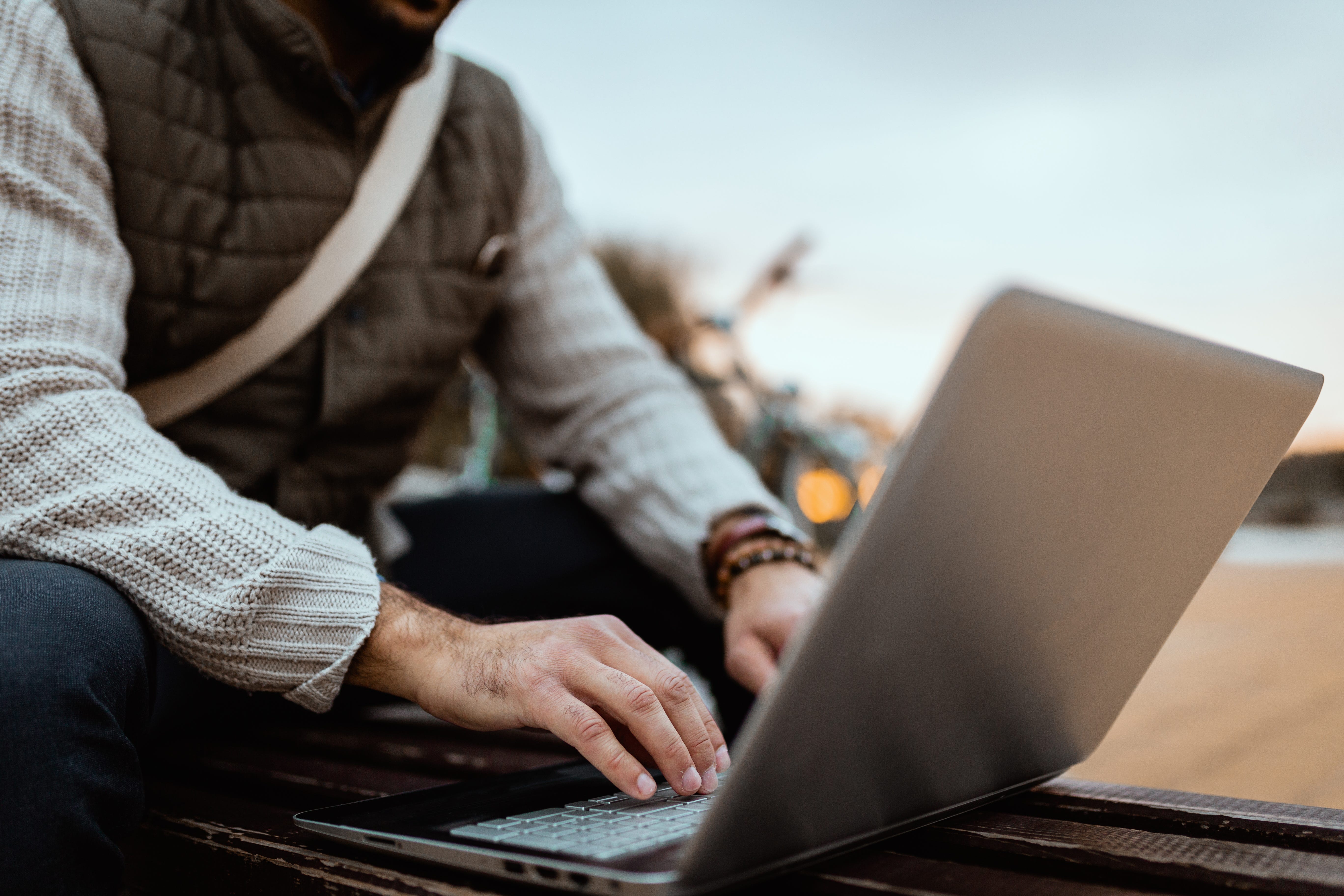 A man wearing a vest types out in his computer.