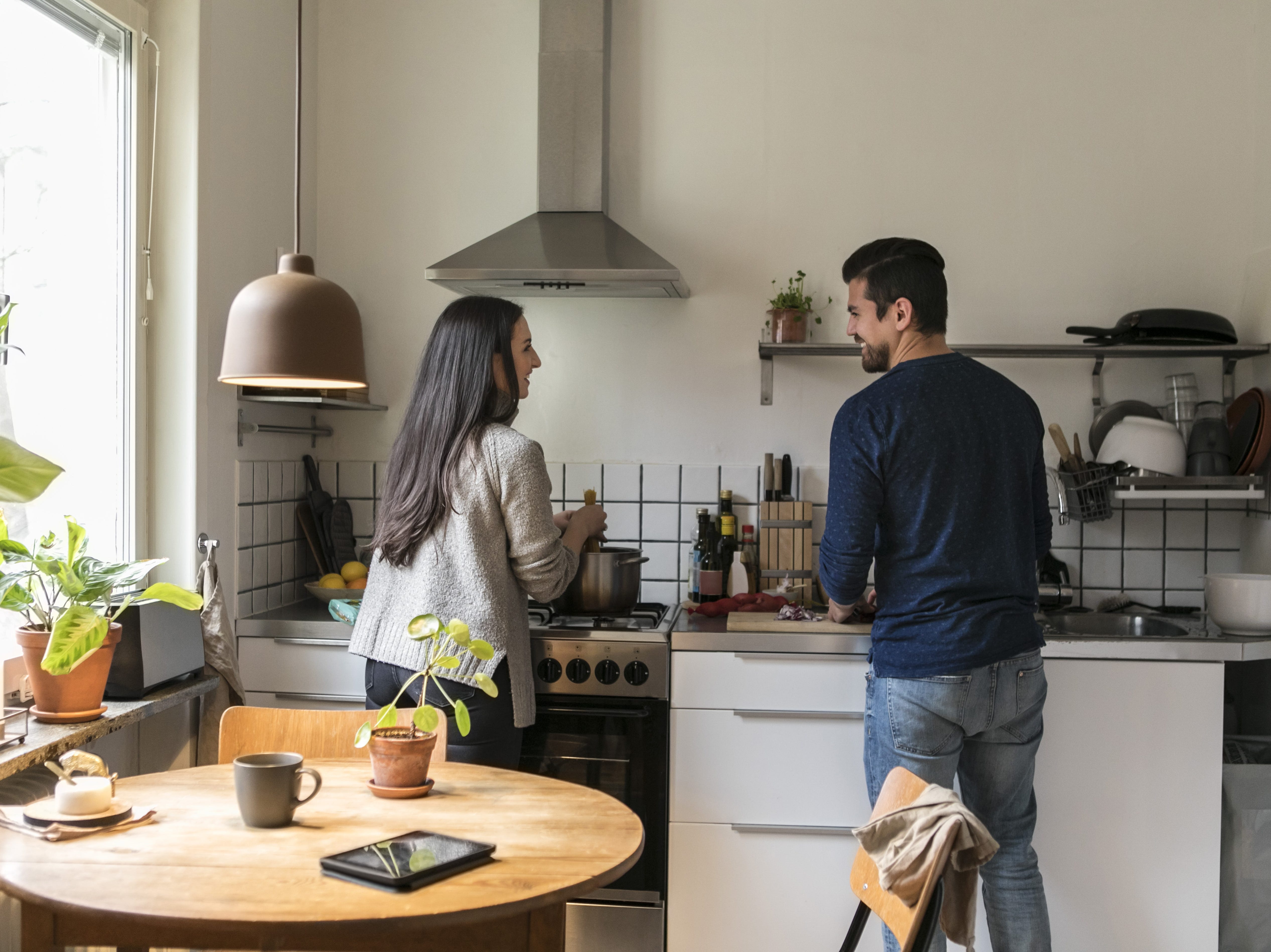 Two people in a kitchen doing chores and talking to each other.