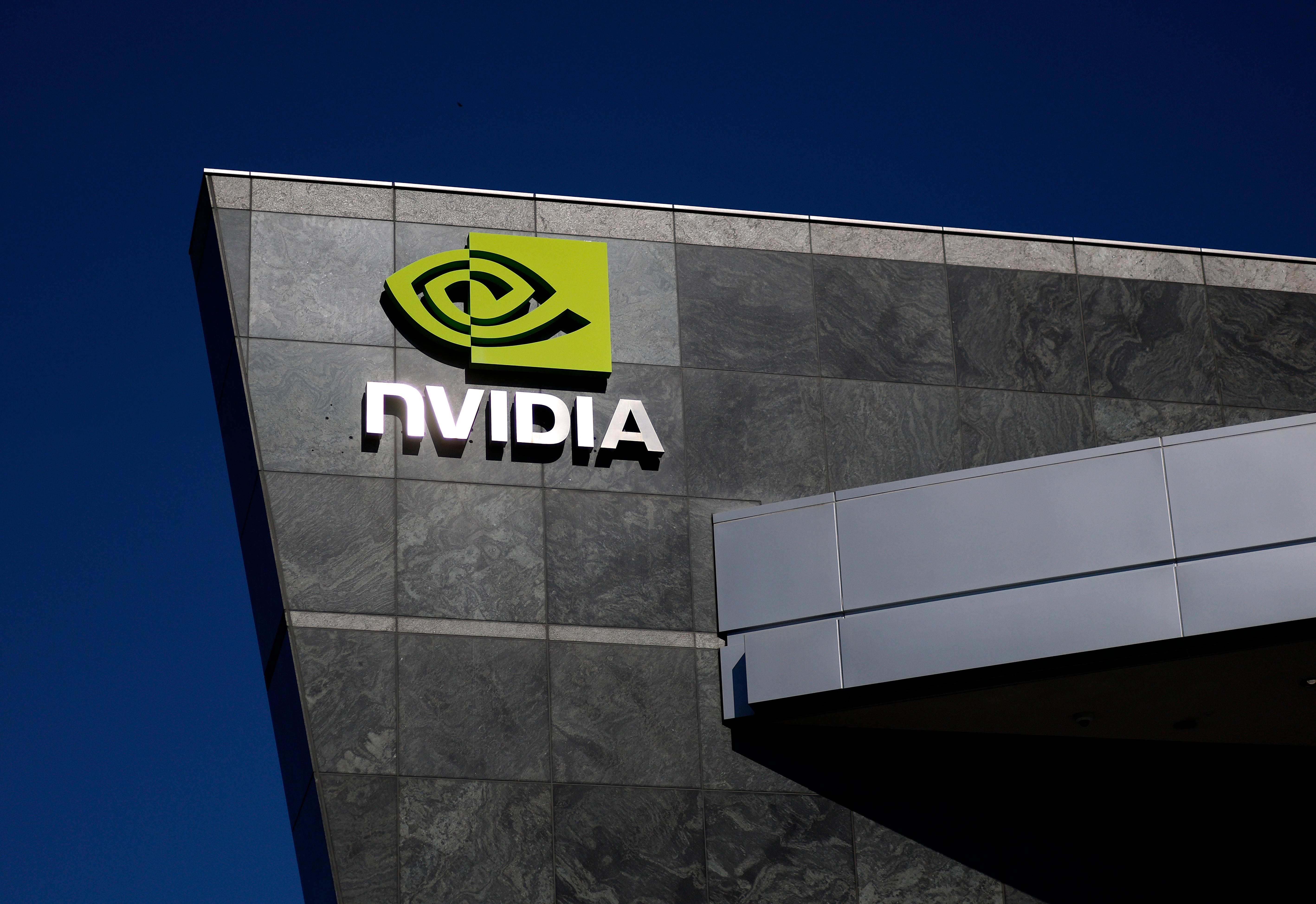 The Nvidia logo, which consists of a green, eye-shaped decal over the company name written in white lettering, is affixed to the side of a black stone building, with a blue sky behind it all.