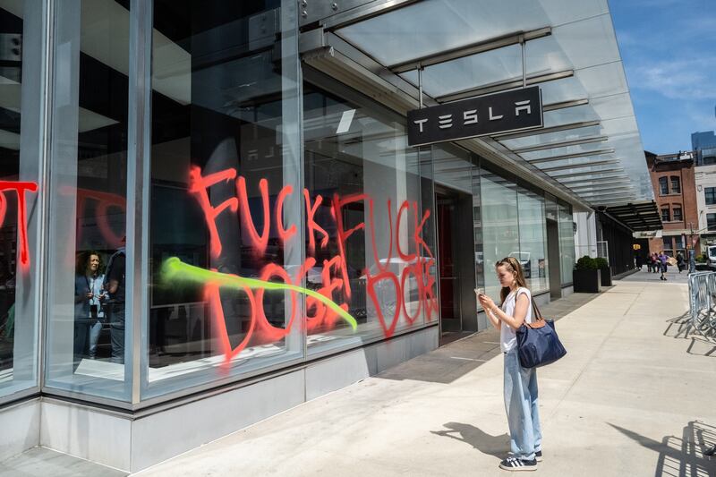 A person walks anti-DOGE messages spray painted on the outside of a Tesla showroom on April 22, 2025 in New York City.