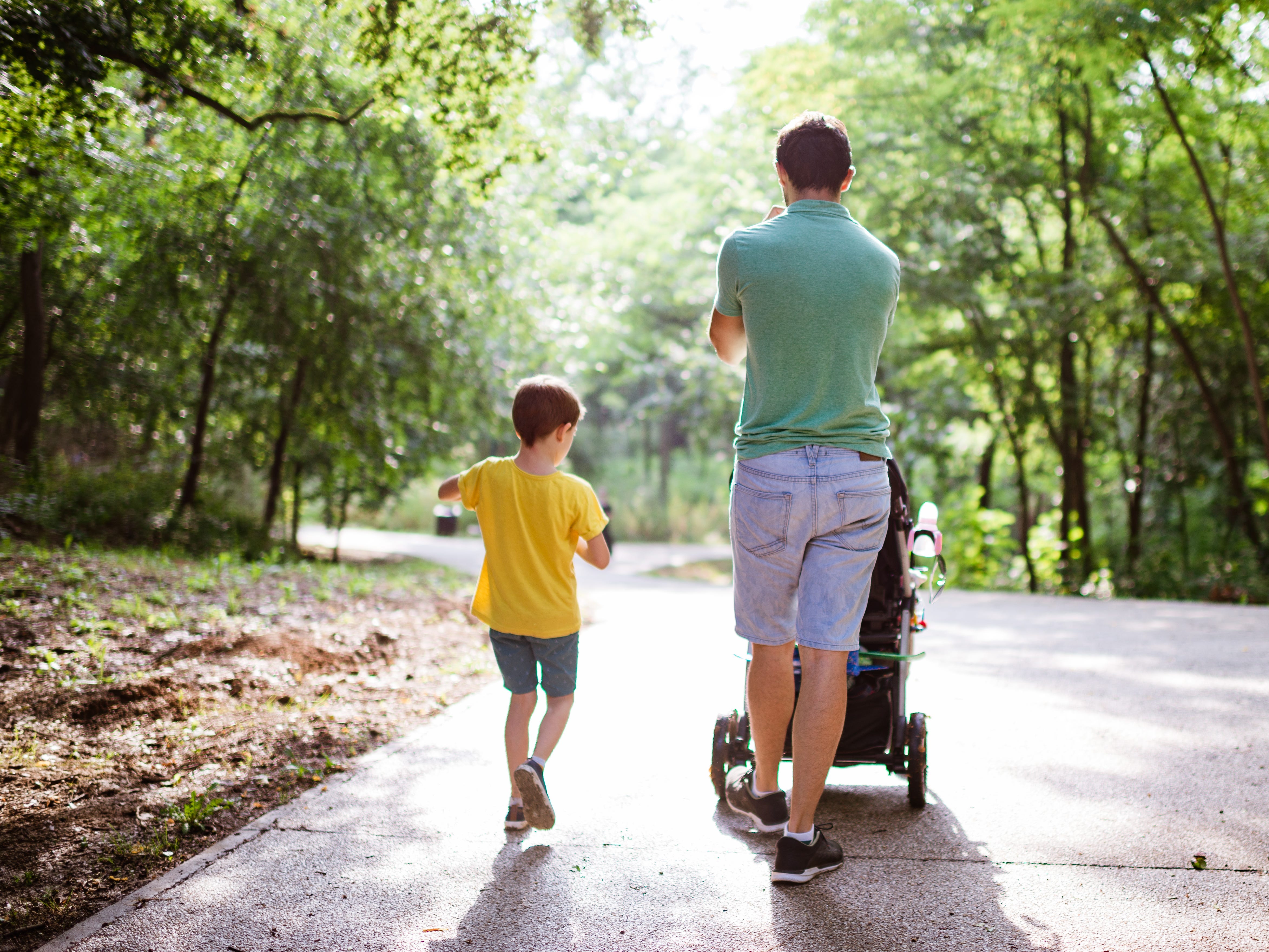 A man pushes a stroller while a young boy walks beside him.