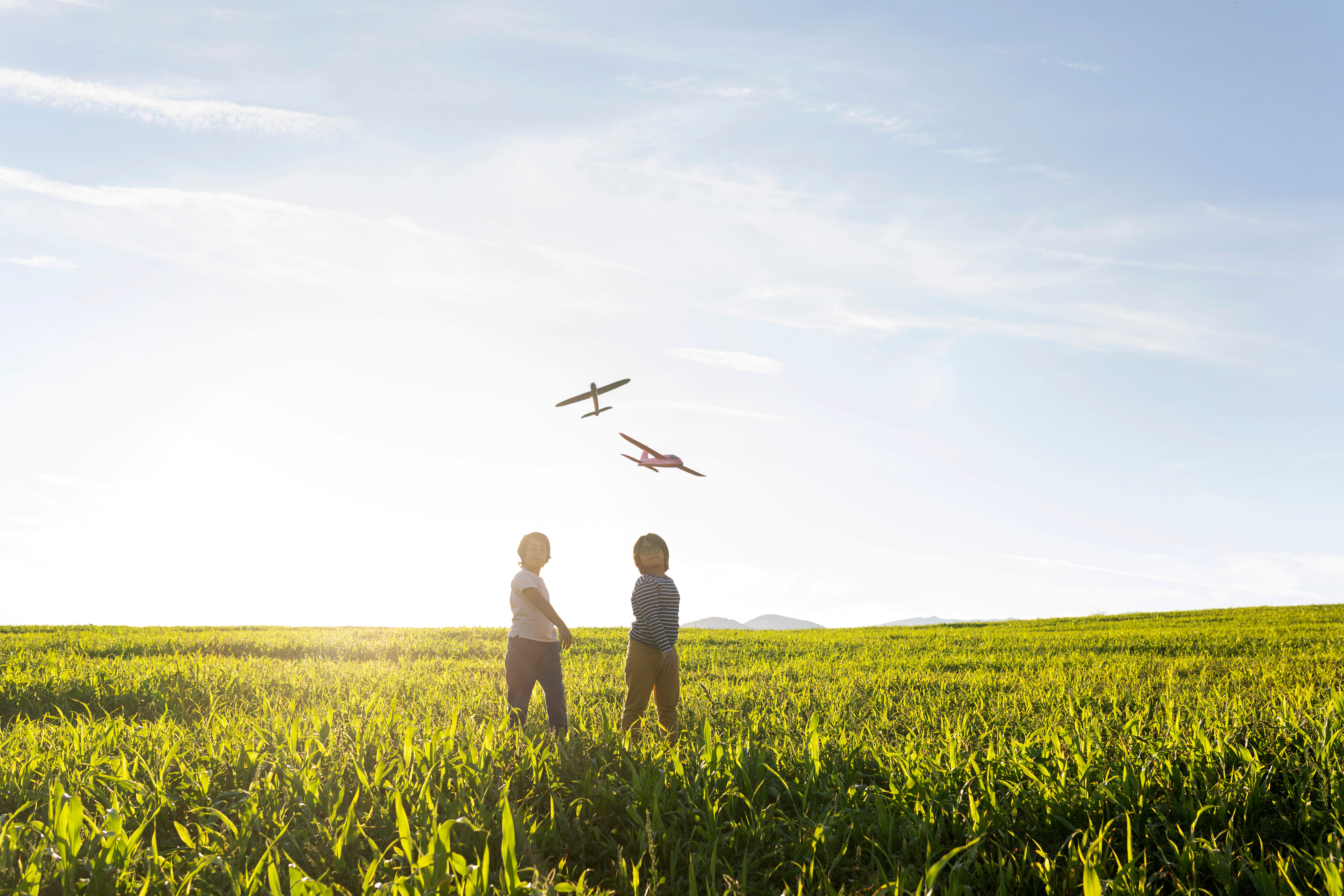 Two children playing with toy planes in a field.