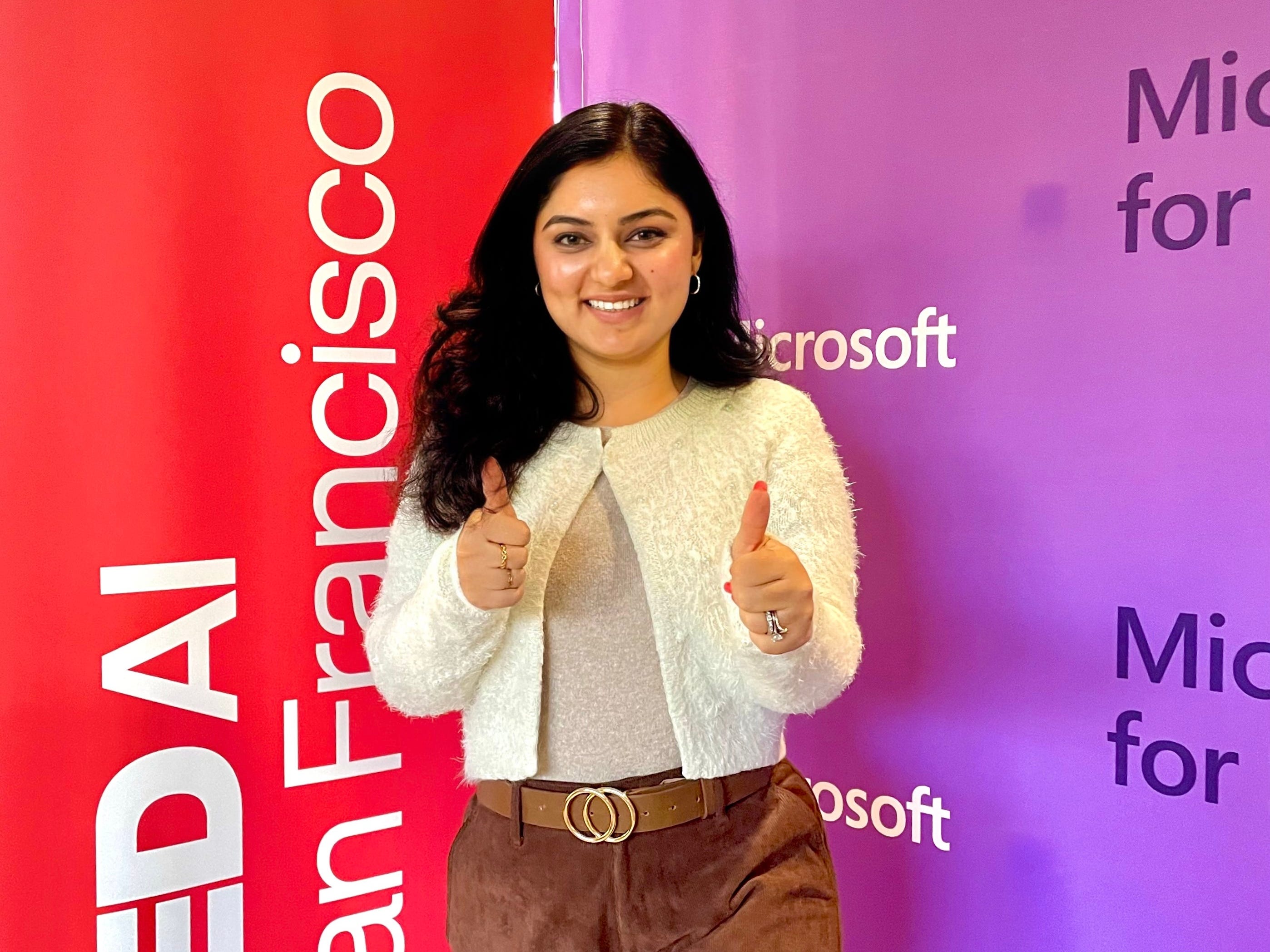 Jigyasa Grover gives two thumbs up as she stands in front of TED AI San Francisco and Microsoft banners