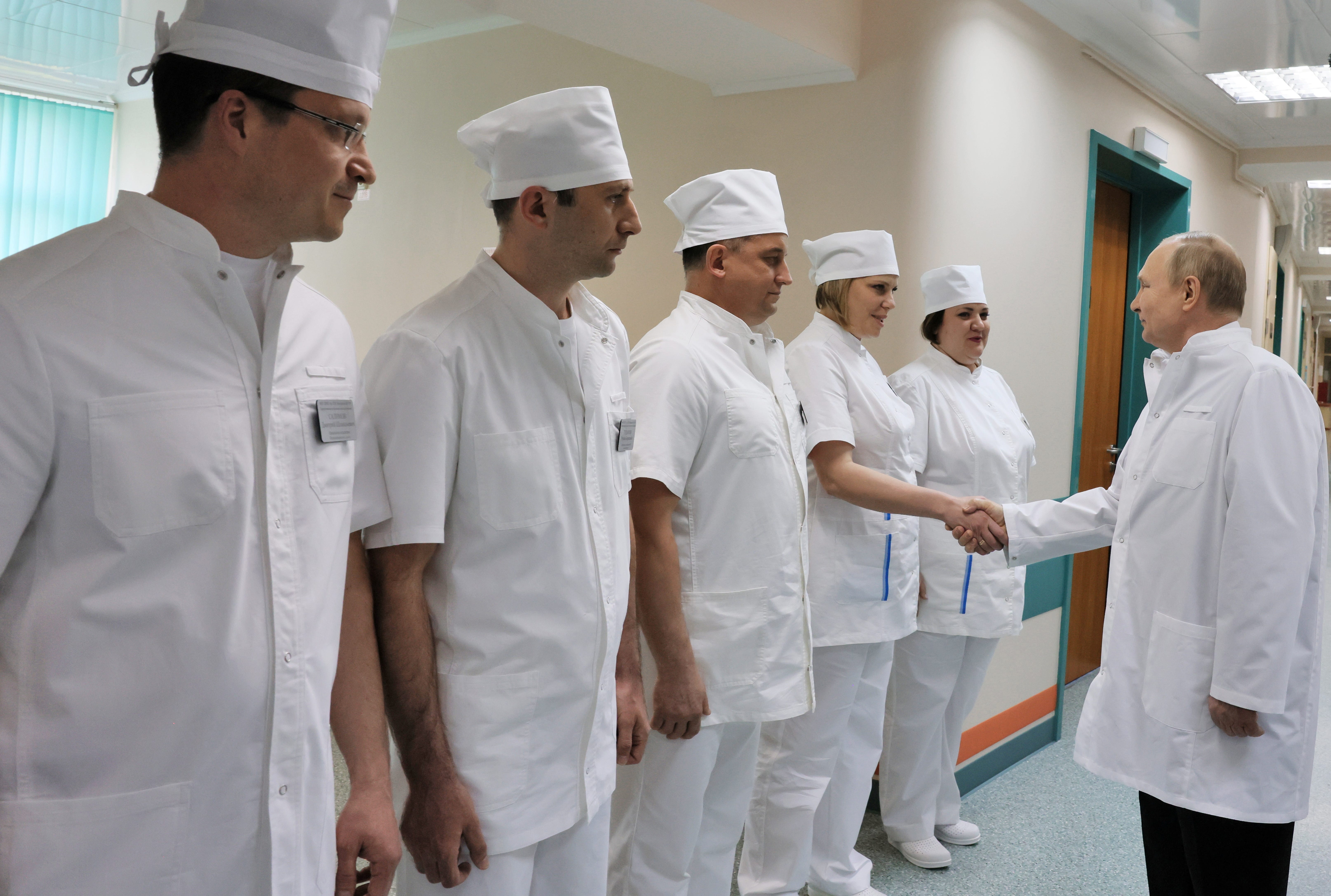 Russian leader Vladimir Putin shakes hands with a medic as he visits soldiers wounded during the conflict in Ukraine at the Mandryk Military Clinical Hospital in Moscow.