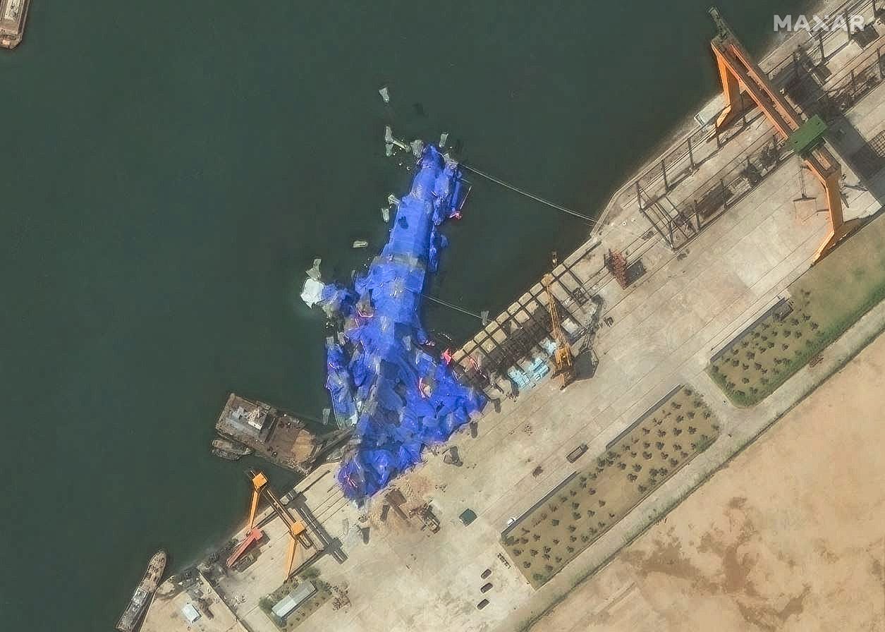 A satellite image showing North Korea's new warship partially submerged in water at a port and covered in blue tarps.