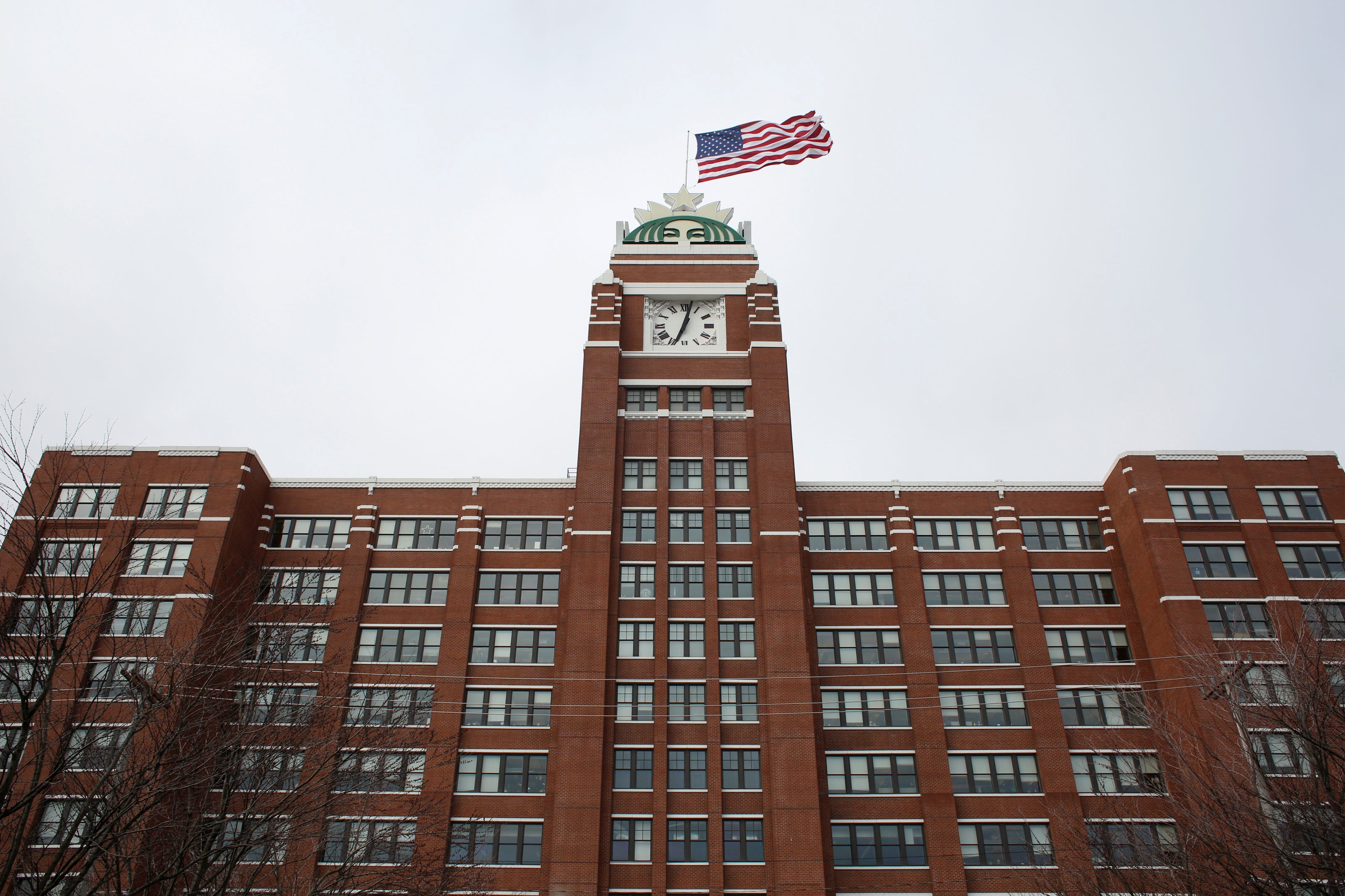 Starbucks company headquarters in Seattle, a red-brick building with a clocktower featuring the coffee chain's Siren mascot and the US flag flying above it, is seen on a cloudy day