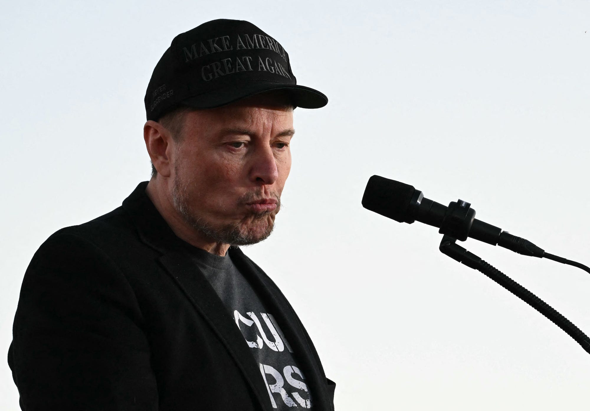 Elon Musk wearing a black "Make America Great Again" hat, black jacket, and a t-shirt that says "Occupy Mars"