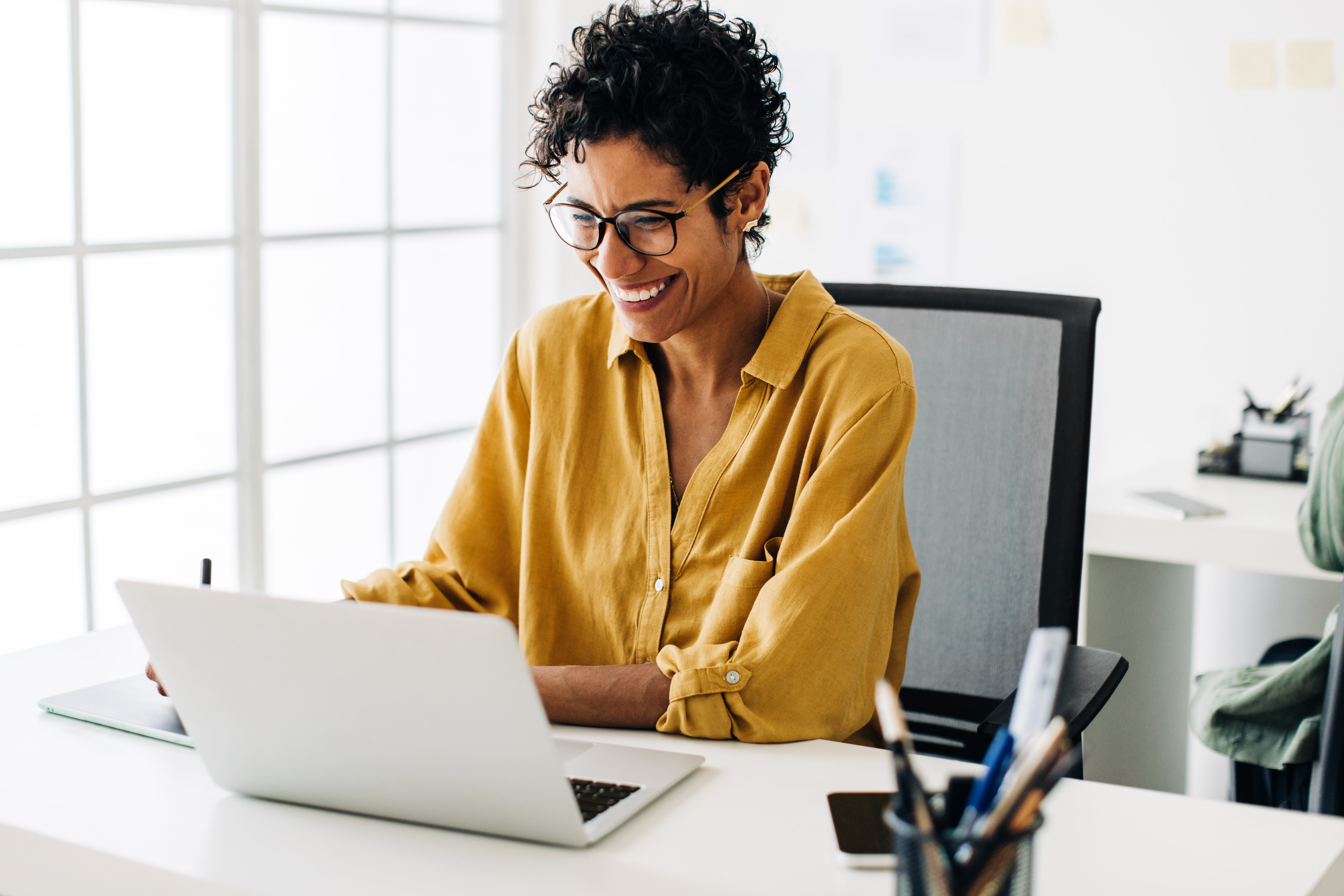 A woman smiling at a computer sat at a desk.