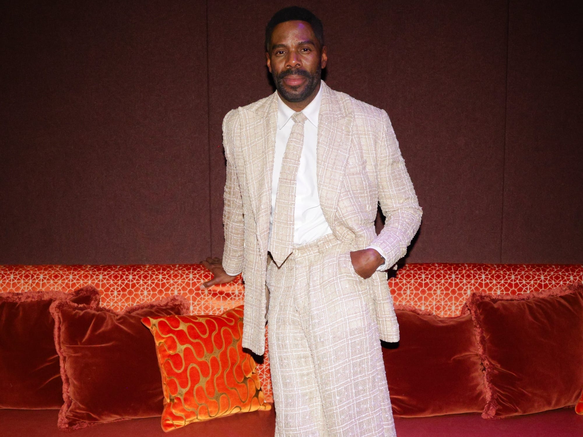 Colman Domingo in a textured suit in front of a red couch.