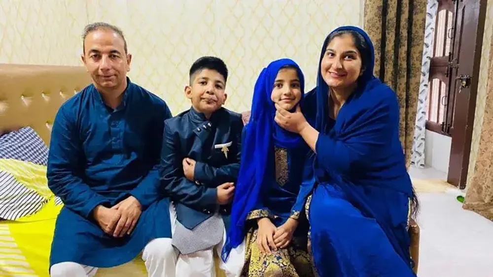 A man, a boy, a girl, and a woman sit for a family photo on a bed. The woman smiles and holds the girl's chin as she smiles.