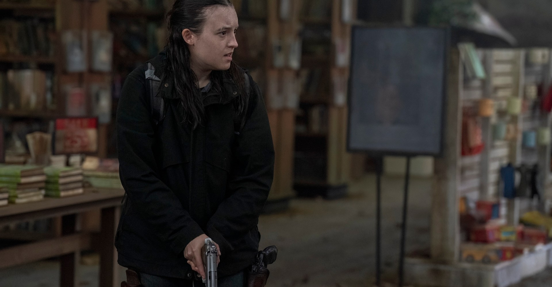 Ellie from The Last of Us show stands in a run-down library, holding a gun