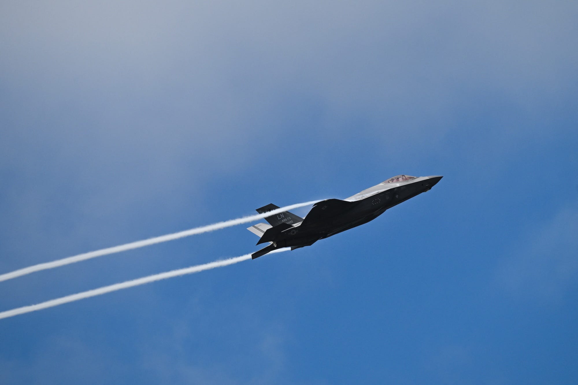 A grey fighter jet in a blue sky with white trails behind it