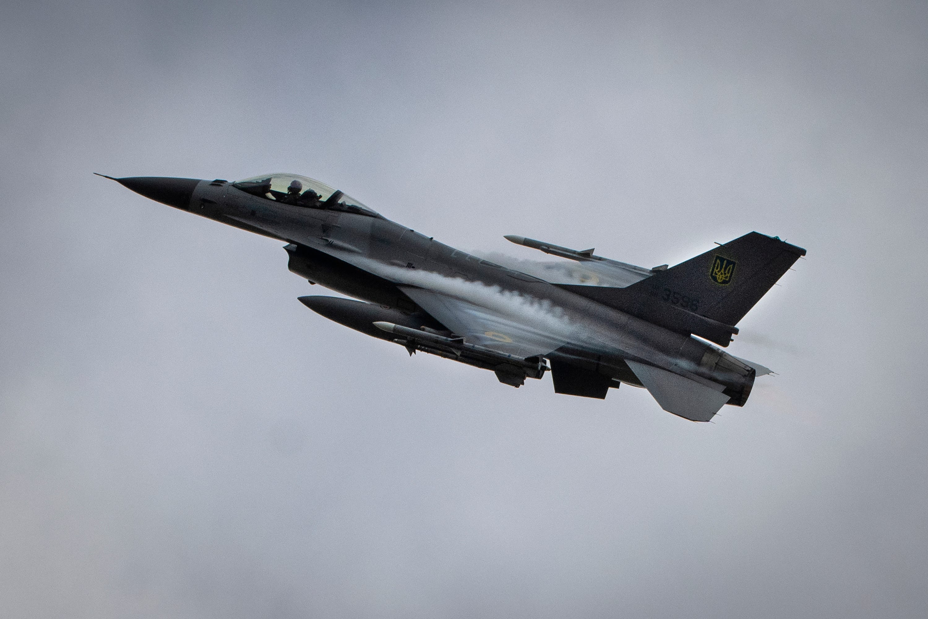 A Ukrainian F-16 flying against grey skies.