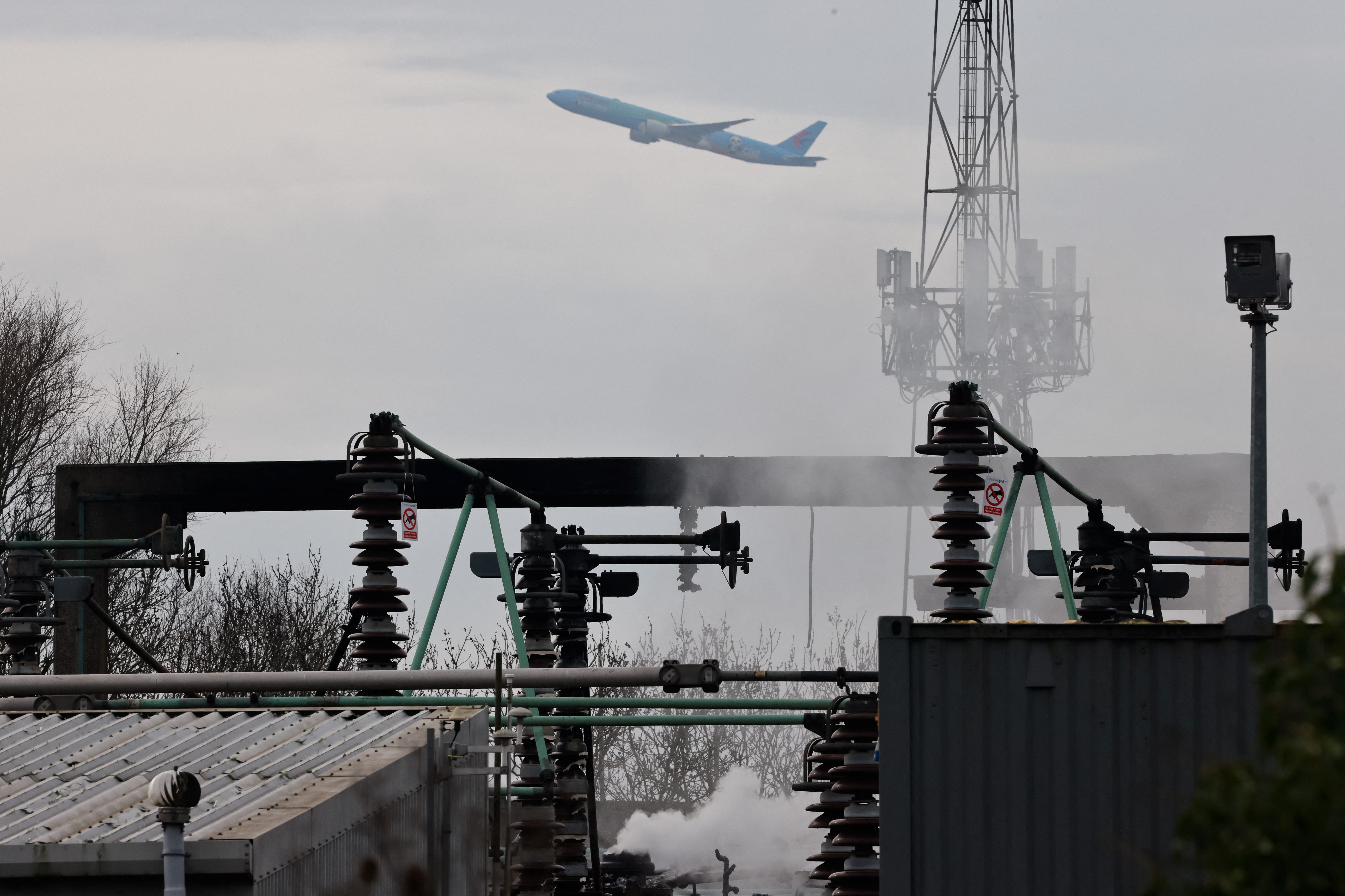 A plane takes off, as smoke rises from an area of an electrical substation a day after it caught fire and wiped out power at Heathrow International Airport, near London, Britain, March 22, 2025.