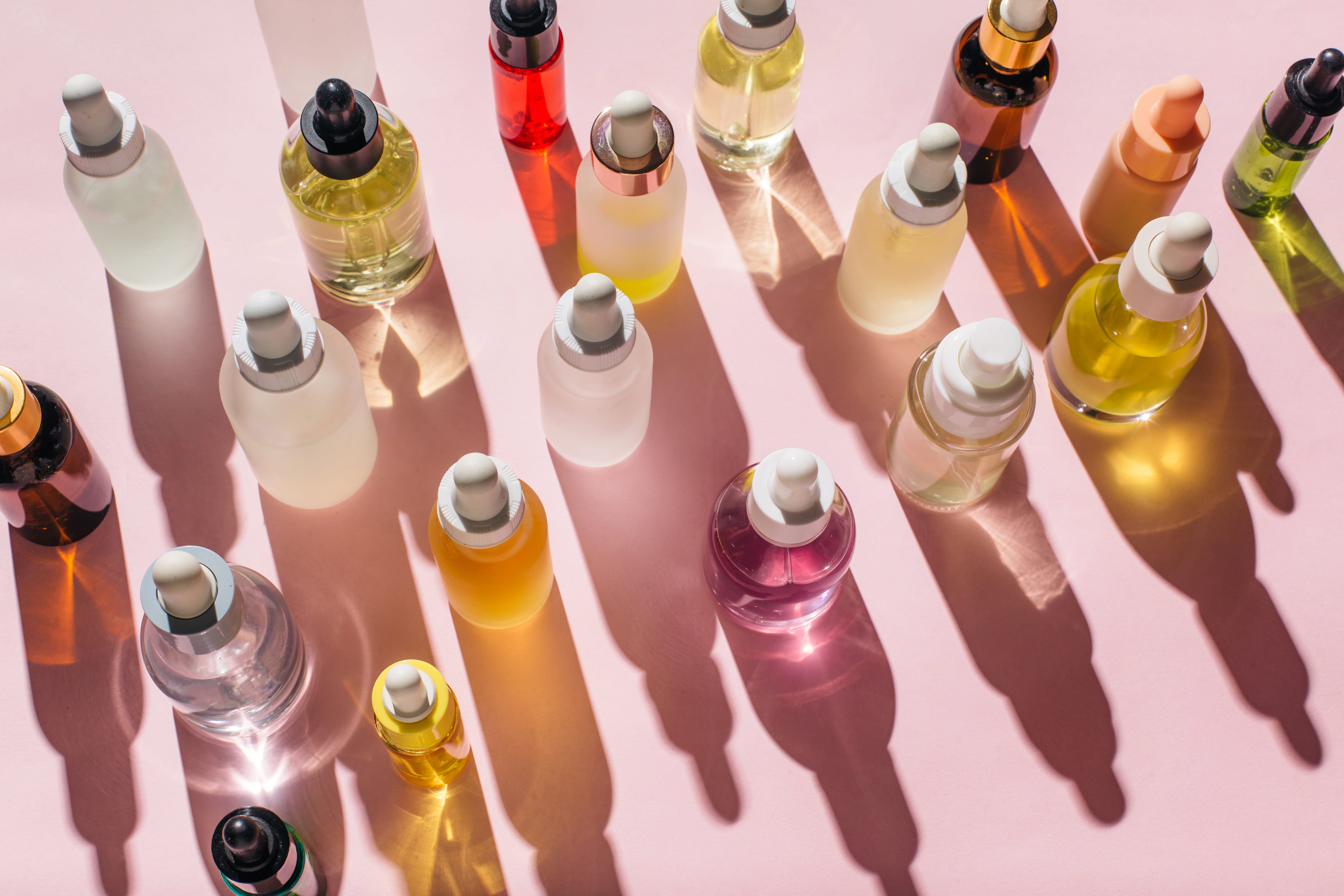 Colorful glass bottles with droppers on a pink background