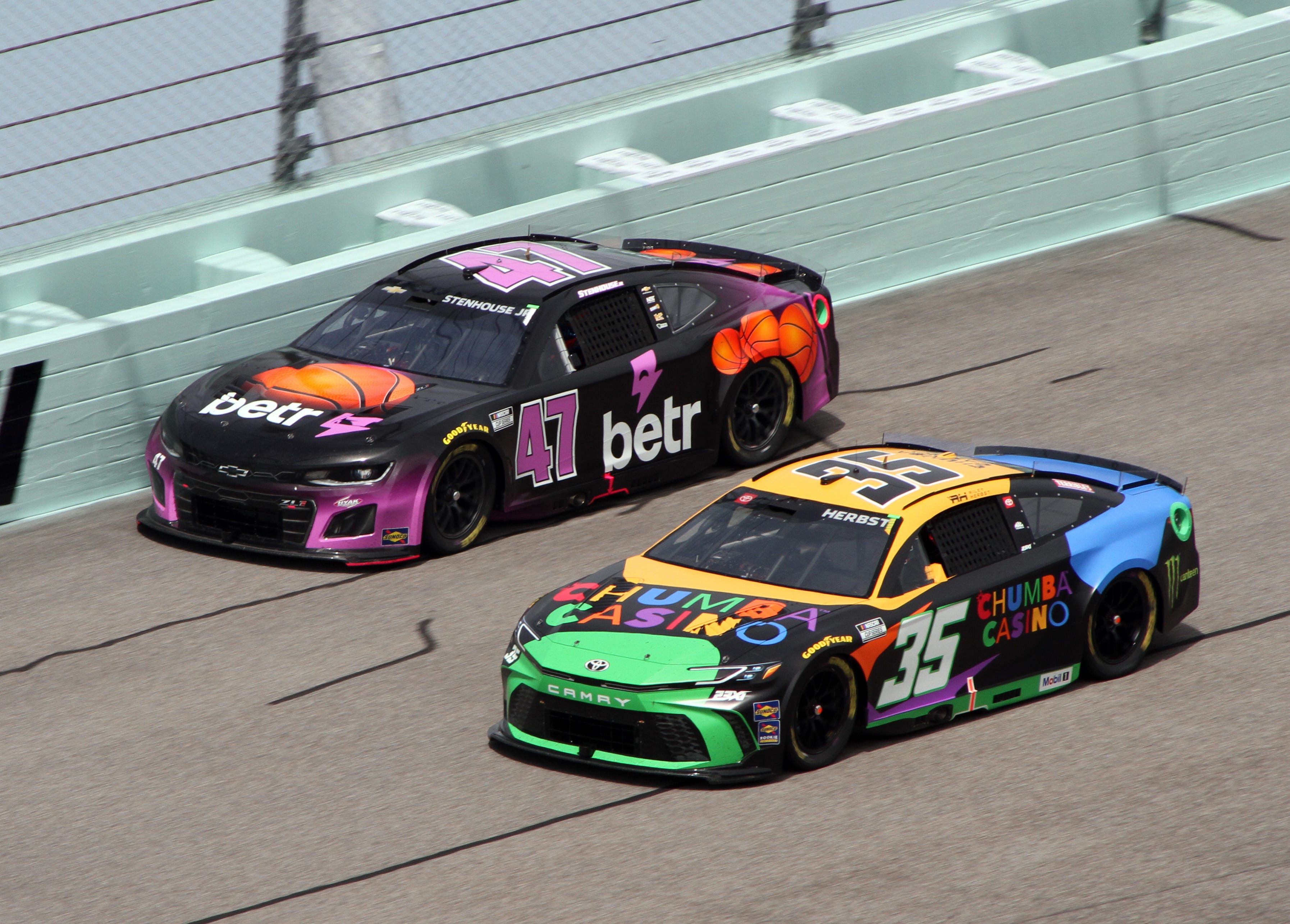 Two NASCAR cars with sponsorships from Betr and Chumba Casino compete on a track.