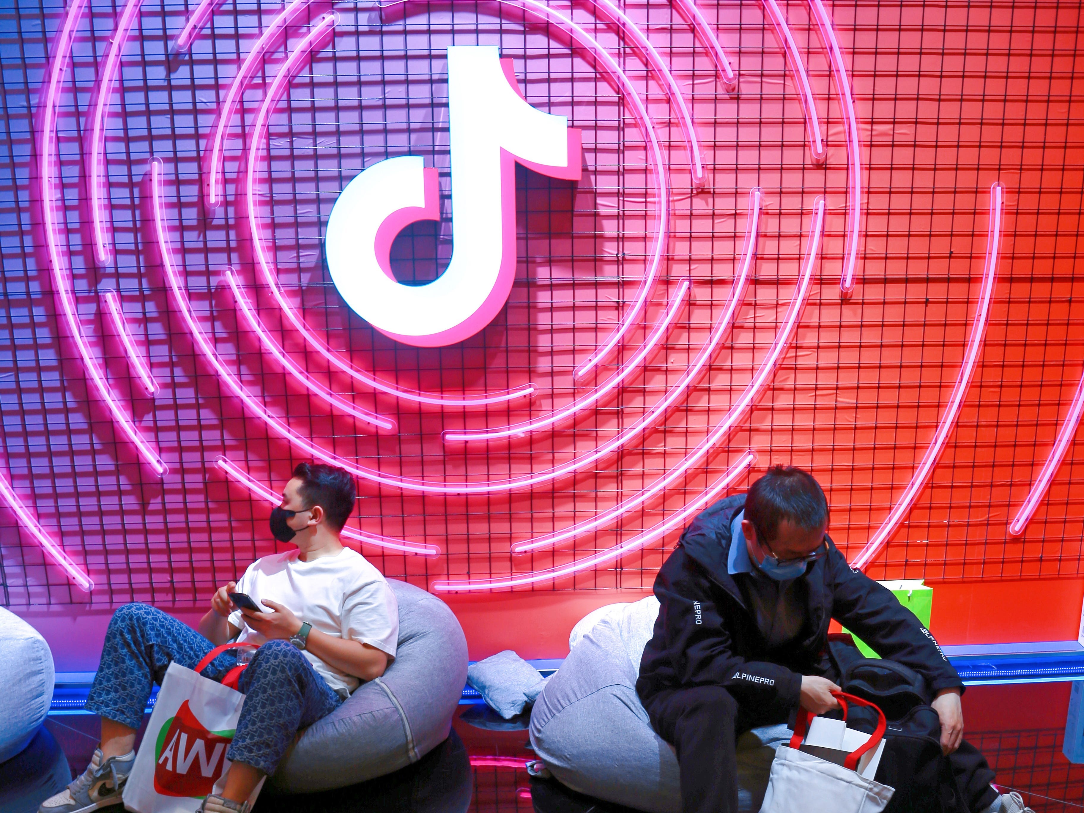 TikTok logo on a purple and red wall with two people sitting underneath it.