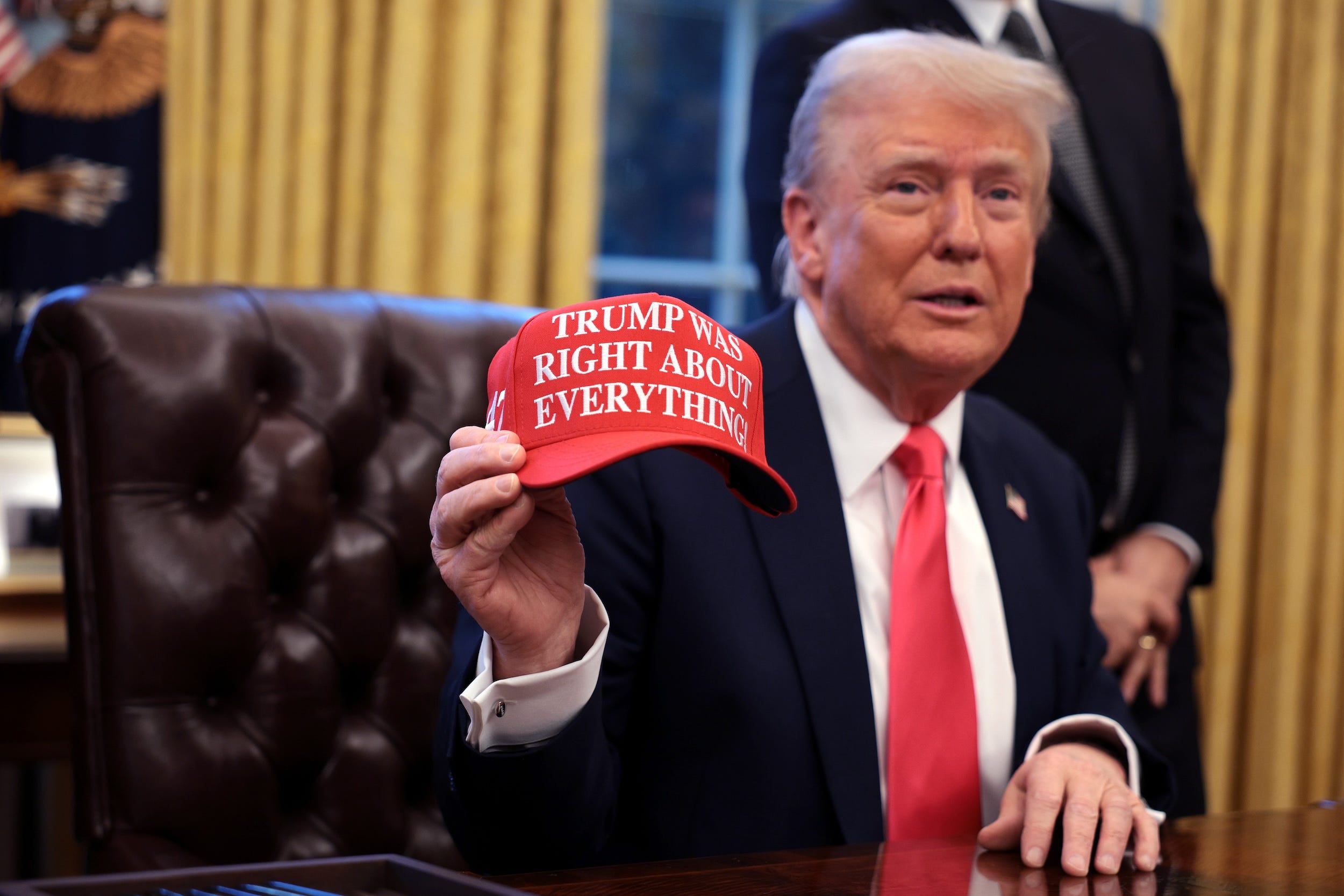 Donald Trump holds up a hat in the Oval Office