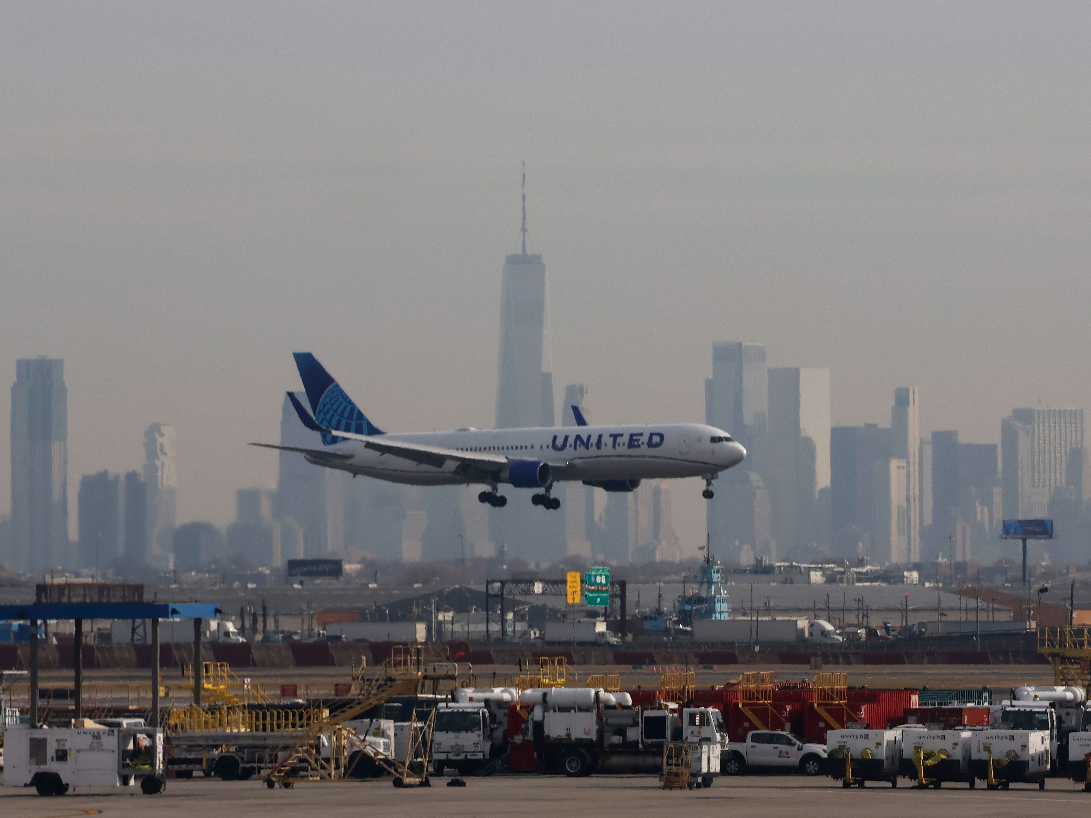 A United Airlines airplane fkying at Newark Liberty International Airport in front of the skyline of lower Manhattan and One World Trade Center in New York City