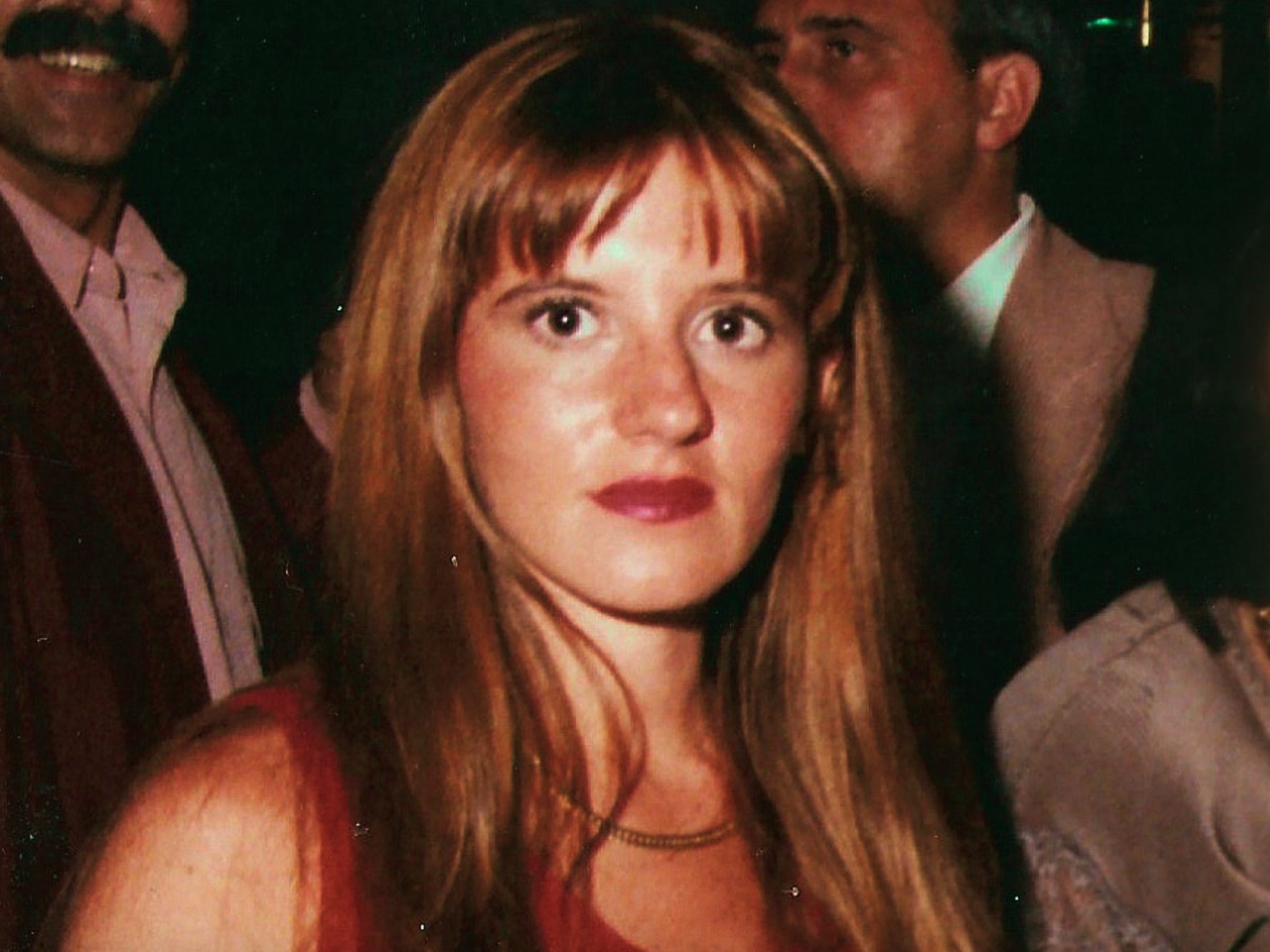 A photo of a young woman with long brown hair and bangs. She has red lipstick on.