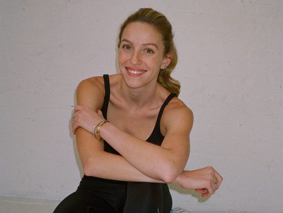 A personal trainer in workout clothes sits on the floor smiling at the camera.