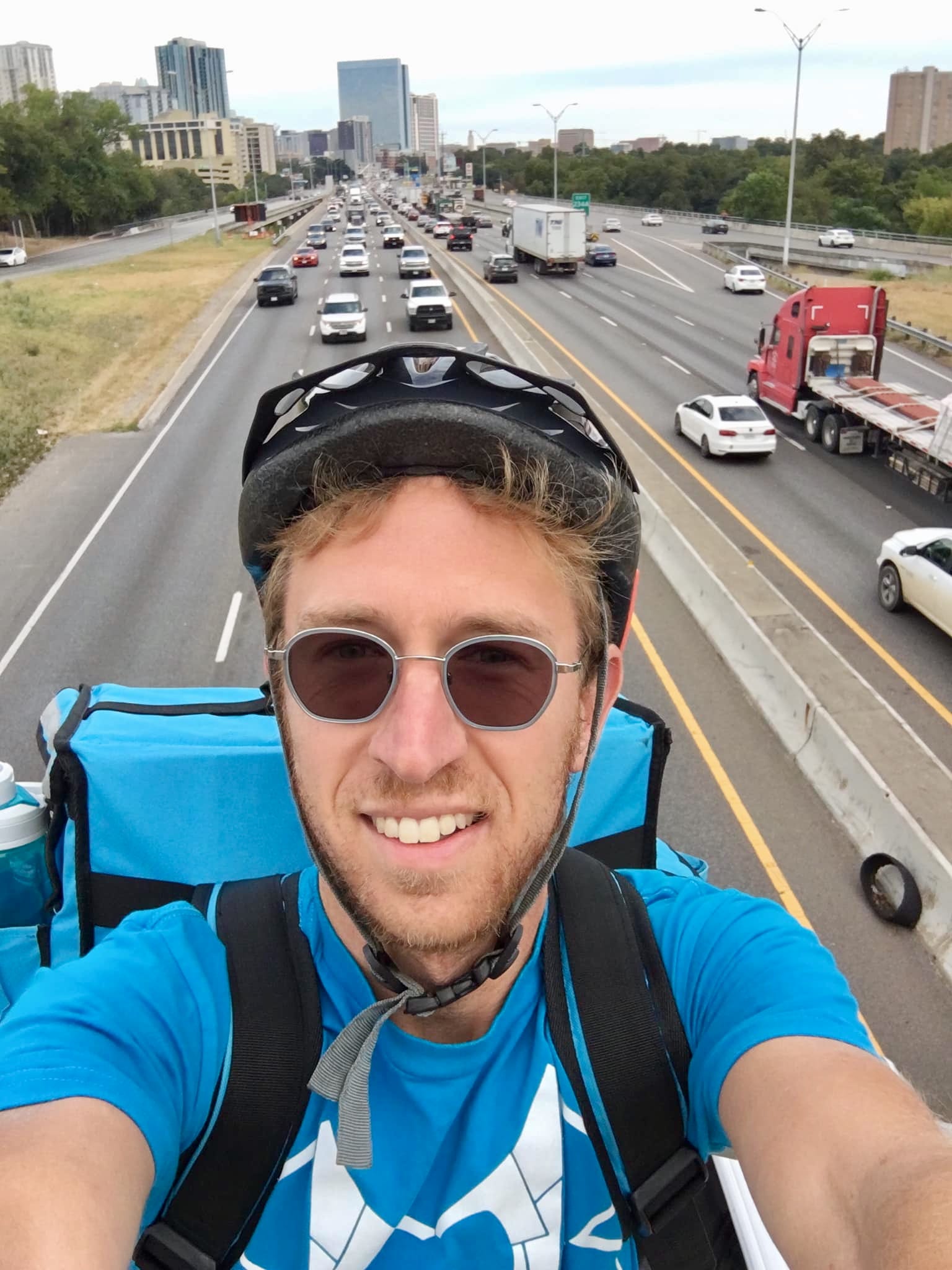 A man wearing a blue delivery rider uniform is taking a selfie.