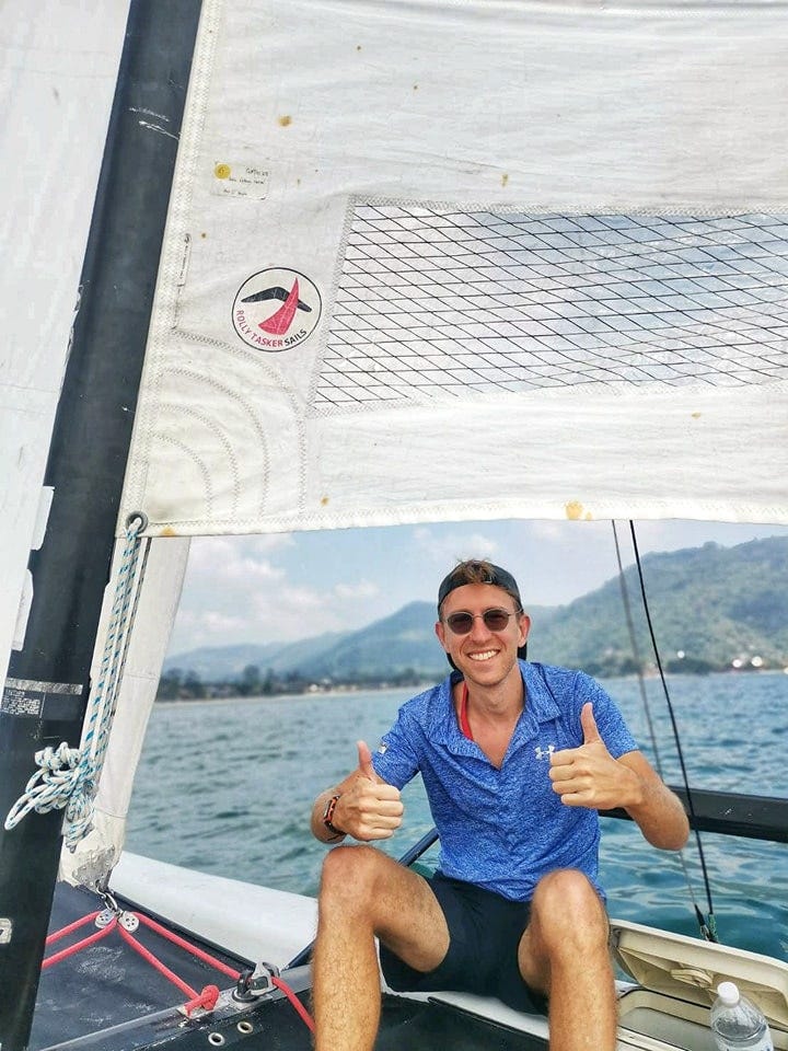A man sitting on a sailboat in Koh Samui, Thailand, giving a thumbs-up sign.