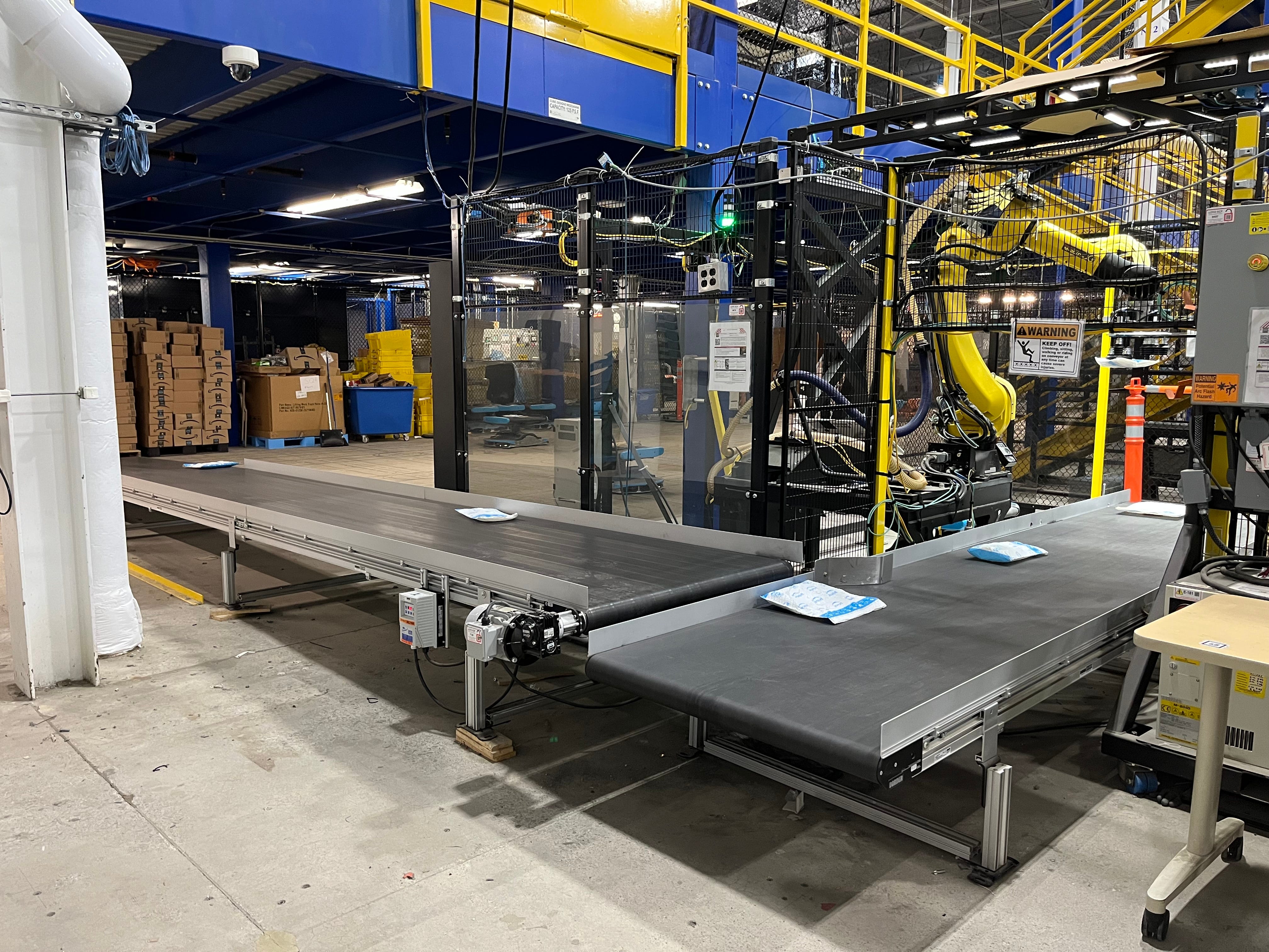 Yellow robotic arm picks up packages in Amazon Robotics facility